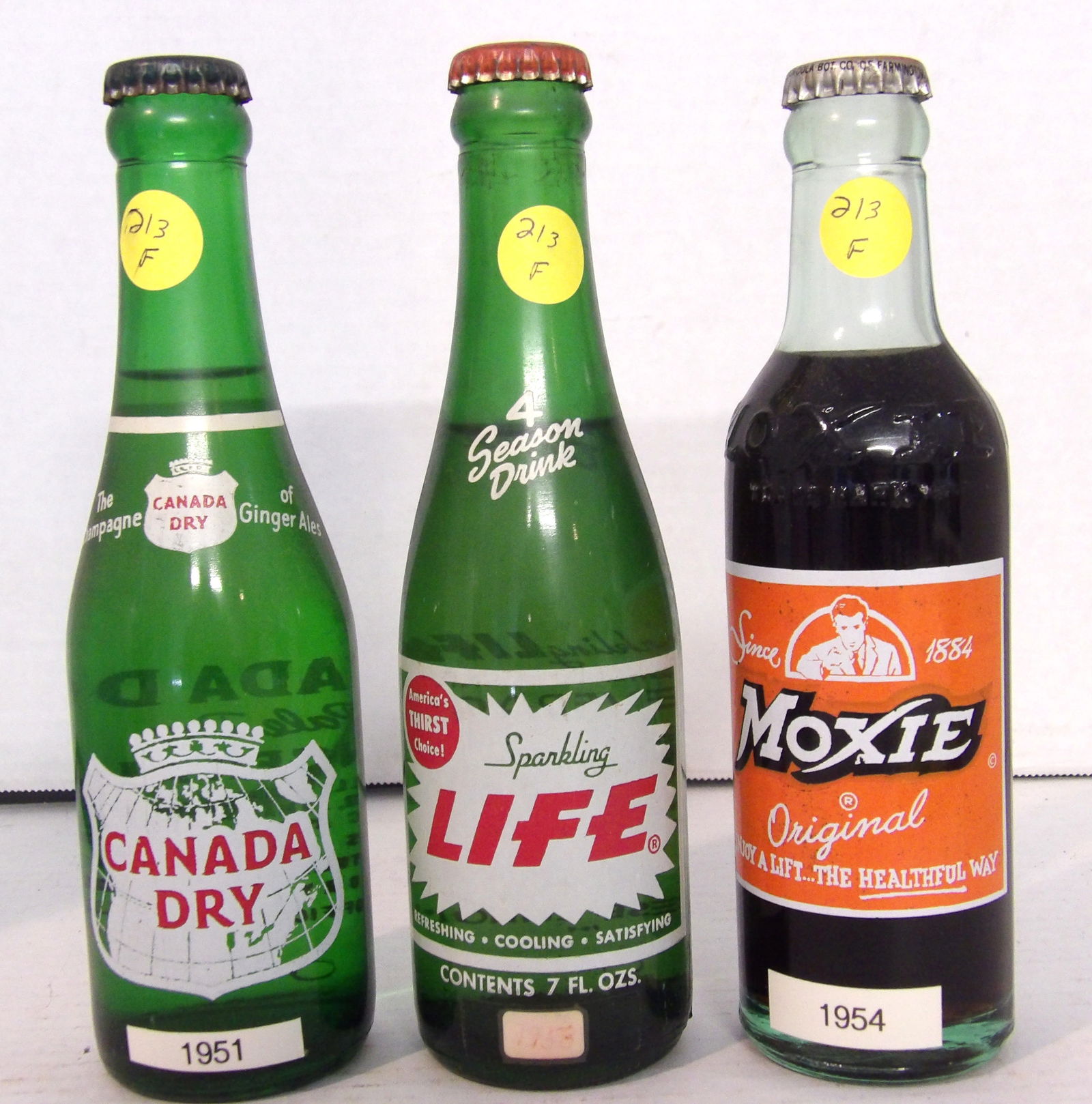 Canada Dry Ginger Ale, Sparking Life, Moxie Soda Vintage Glass Bottles: This trio of vintage glass bottles includes a 1951 Canada Dry Ginger Ale (sealed w/ original contents), a 1958 Sparking Life (sealed w/ original contents), and a 1954 Moxie Soda (sealed w/ original co