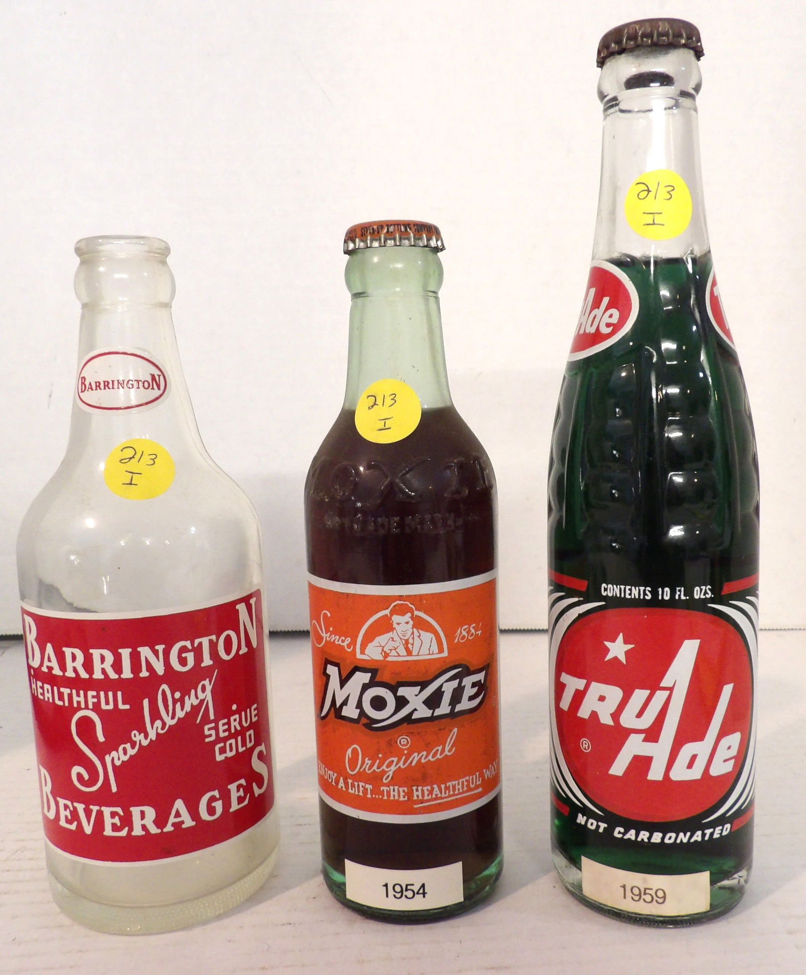 Tru Ade Grape, Moxie, Barrington Glass Soda Bottles: This trio of vintage glass soda bottles includes a 1959 Tru Ade Grape (sealed w/ original contents), a 1954 Moxie (sealed with original contents), and a Barrington Sparking Beverage (open / empty. No