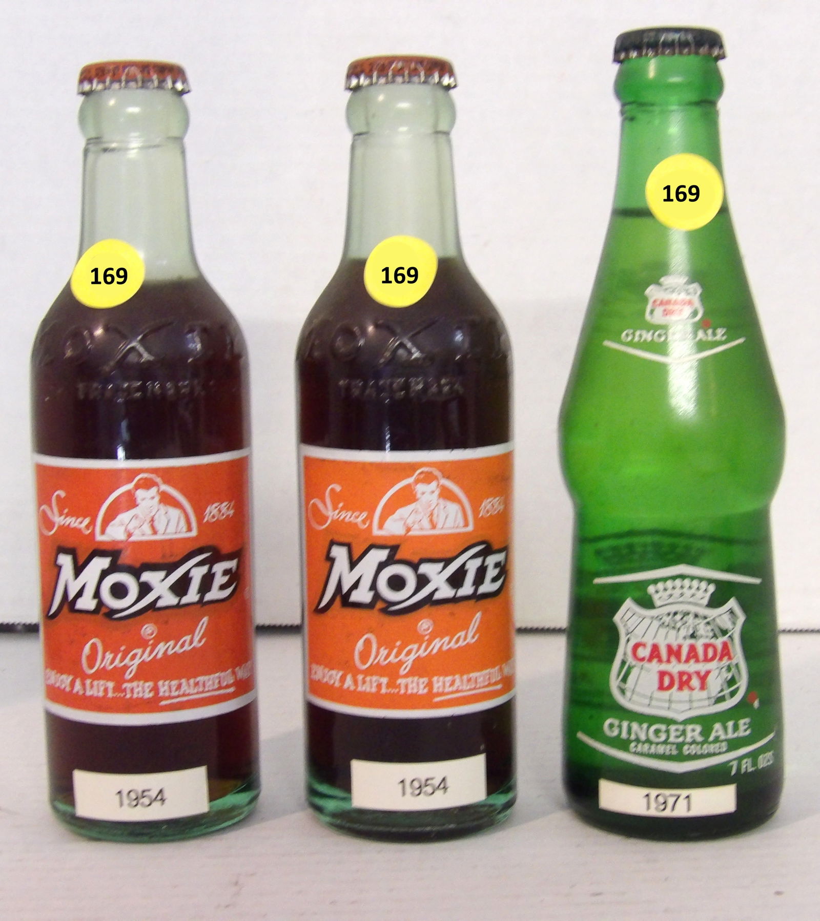 Moxie & Canada Dry Vintage Soda Glass Bottles (3 pcs): This group of vintage glass bottles are sealed (contains original contents). Group includes two Moxie (1954), and one Canda Dry Ginger Ale (1971). 8"