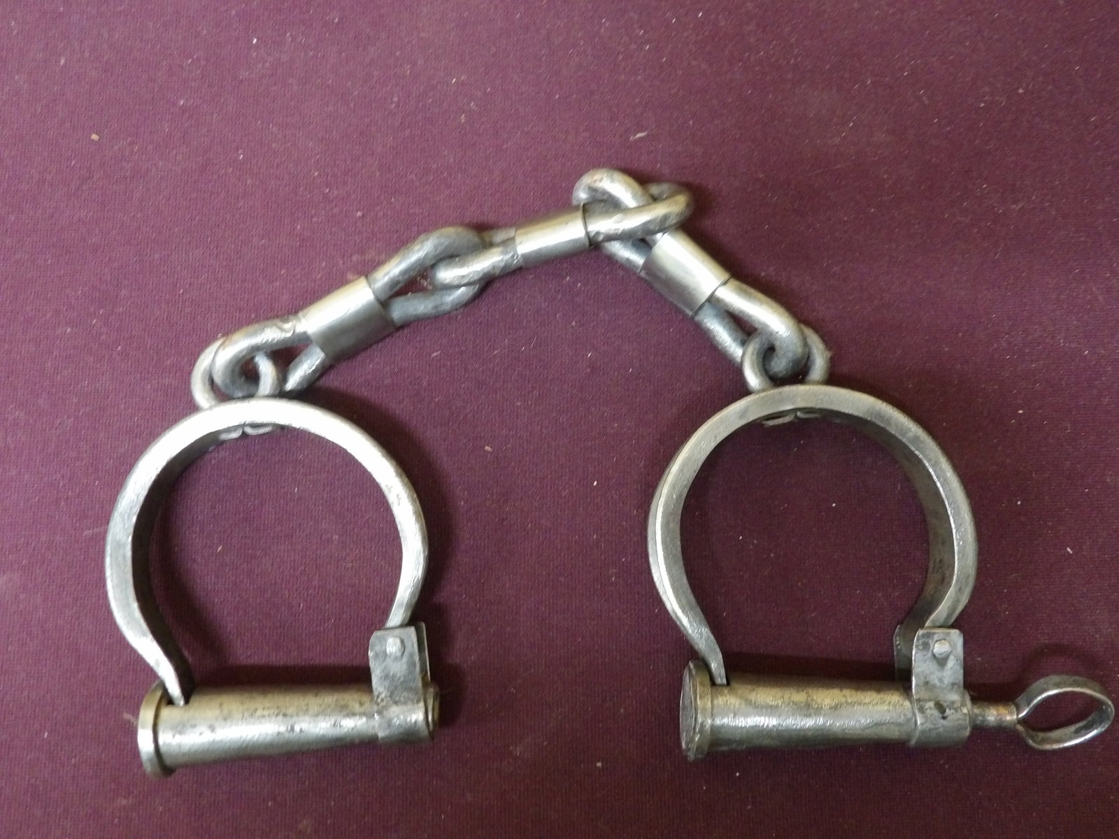 Civil War Era Darby Handcuffs w/ Key: This pair of antique iron Darby-style handcuffs feature a fixed, non-adjustable design with a single central chain connecting the two cuffs. Includes key.