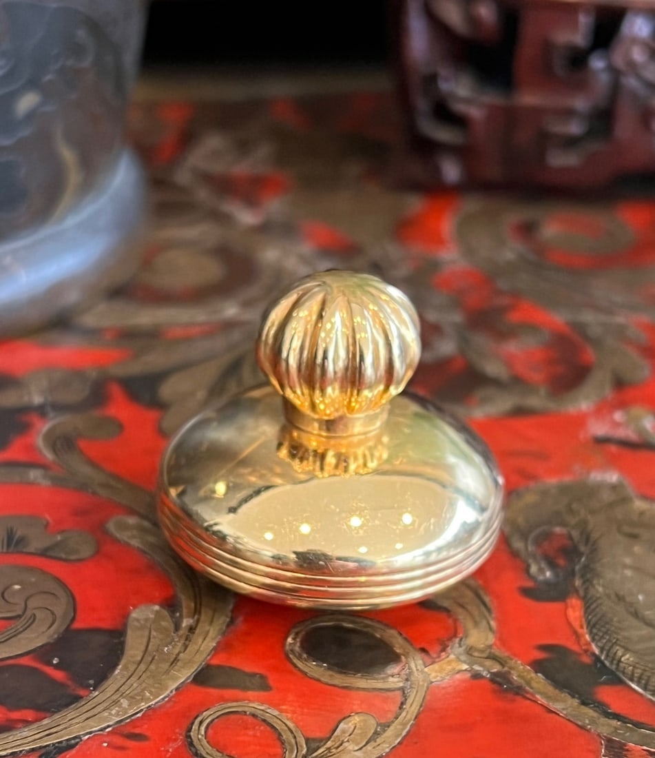 AN 18CT GOLD PILL BOX: AN 18CT GOLD PILL BOX AN 18CT GOLD PILL BOX the 18 carat gold box or scent bottle of small size, with fluted lid, on a circular base, marked 750 to the underside, 31 grams in weight 3cm high