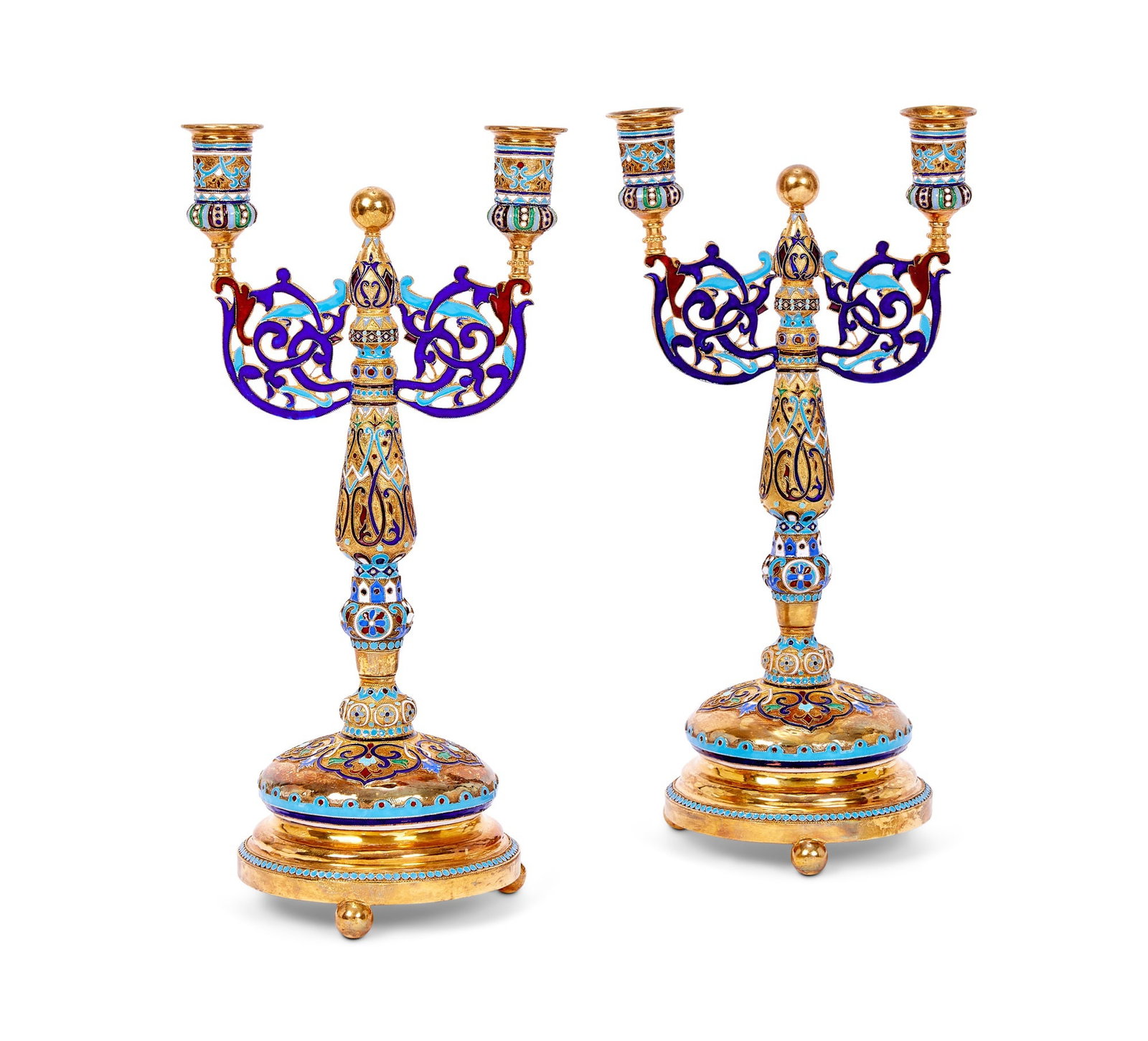 A PAIR OF SILVER GILT AND CHAMPLEVE ENAMEL CANDELABRA IN THE RUSSIAN STYLE: A PAIR OF SILVER GILT AND CHAMPLEVE ENAMEL CANDELABRA IN THE RUSSIAN STYLE richly decorated throughout with polychrome enamelling, the removable candle holders raised on pierced, scrolling branches, c