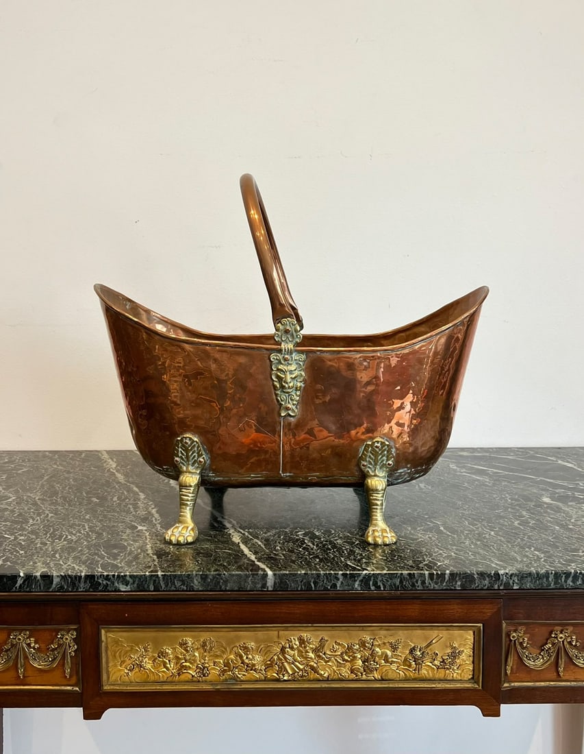A 19TH CENTURY COPPER AND BRASS LOG BASKET: A 19TH CENTURY COPPER AND BRASS LOG BASKET the bin or bucket of boat shaped form, raised on four brass paw feet, with swing handle over, 47cm wide x 27cm high handle down
