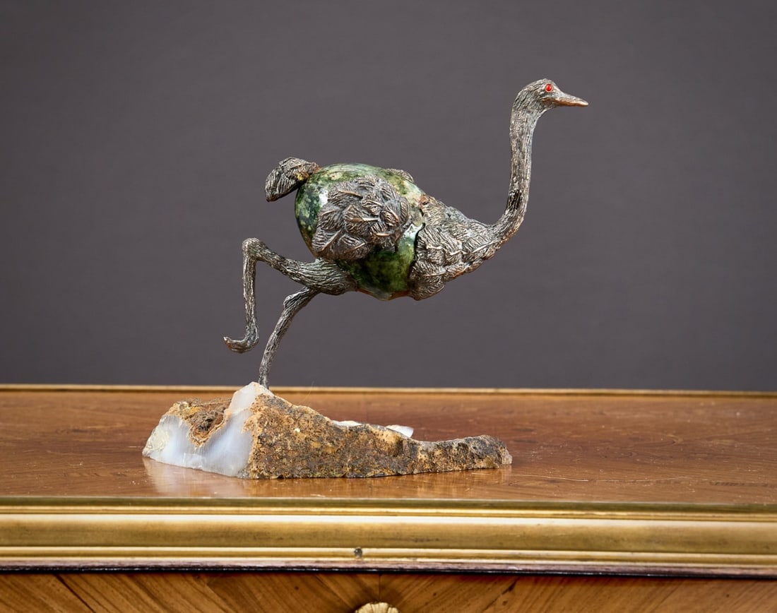 AN AGATE AND MALACHITE MODEL OF A RUNNING OSTRICH: AN AGATE AND MALACHITE MODEL OF A RUNNING OSTRICH the bird with inset red eyes, with silvered metal head, legs and wings and malachite egg shaped body, on an agate geode rocky base, 14cm high