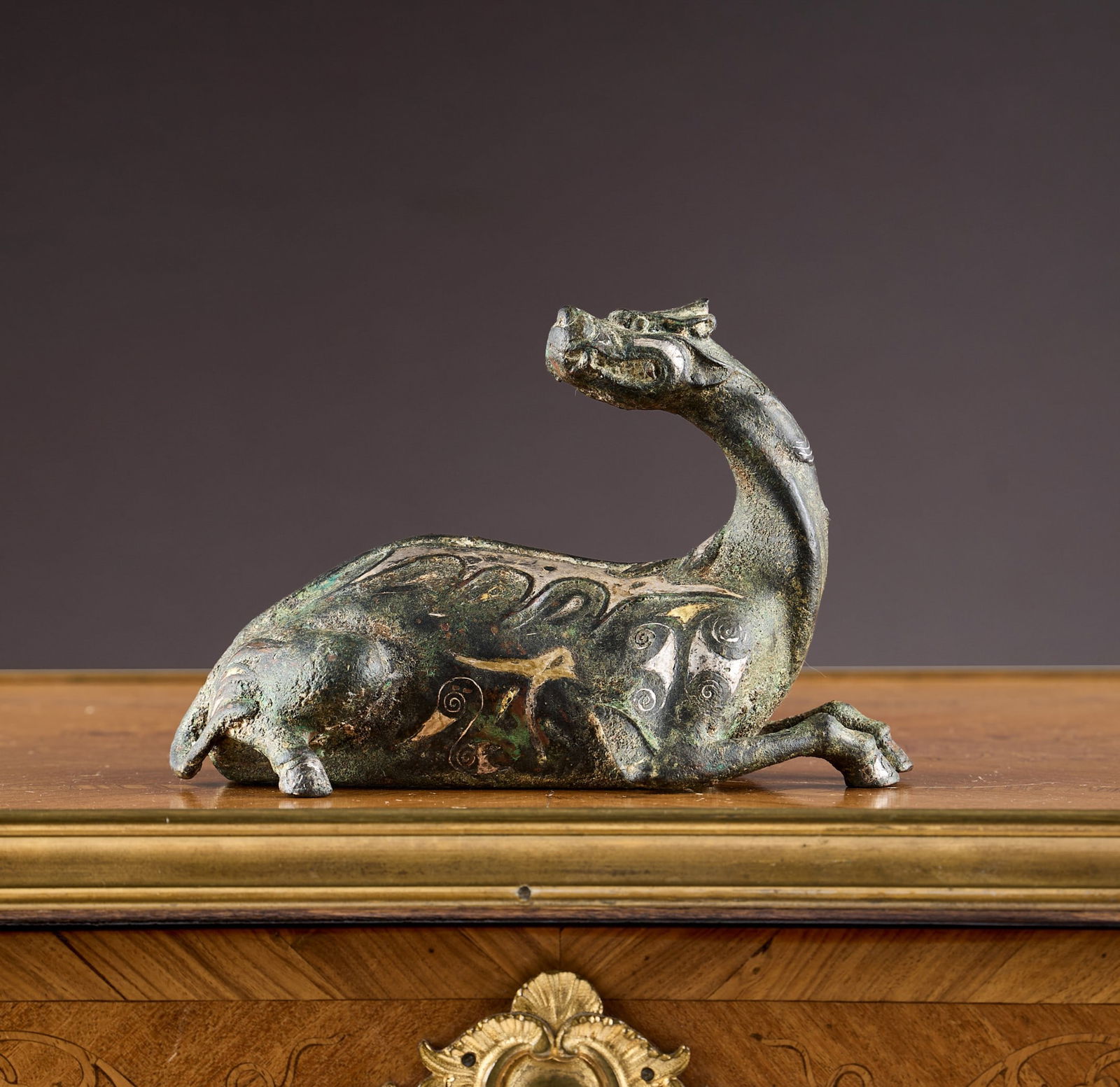 A CHINESE GOLD AND SILVER INLAID BRONZE DEER, PROBABLY QING DYNASTY: A CHINESE GOLD AND SILVER INLAID BRONZE DEER, PROBABLY QING DYNASTY in the Warring States style, the recumbant deer decorated with archaic motifs, the bronze body with extensive verdi gris, 16cm wide