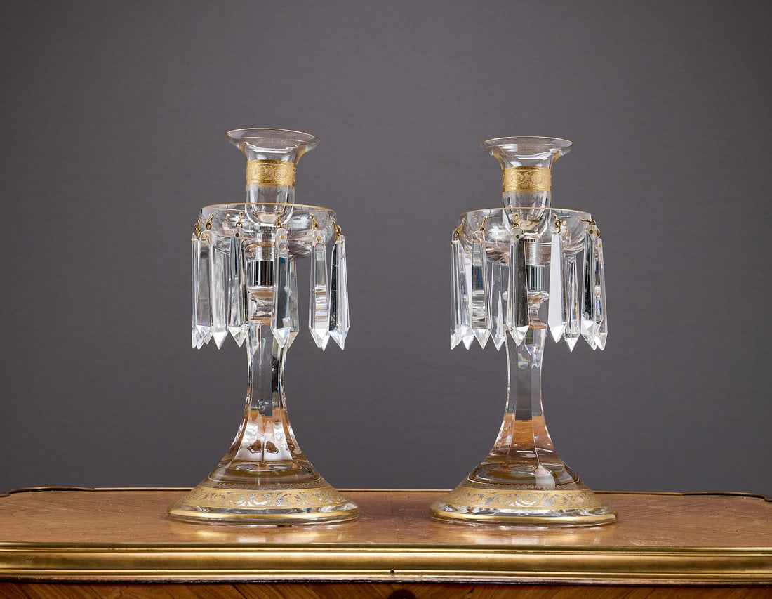 ST LOUIS: A PAIR OF GILT DECORATED CRYSTAL GLASS CANDLESTICK LUSTRES: ST LOUIS: A PAIR OF GILT DECORATED CRYSTAL GLASS CANDLESTICK LUSTRES with urn shaped nozzles over drip pans hung with prismatic drops, on faceted stems and circular feet, with gilt acanthus decoration