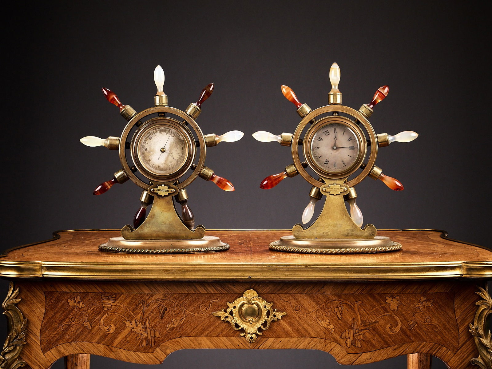 A RARE SET OF 19TH CENTURY ENGLISH AGATE MOUNTED DESK CLOCK AND BAROMETER BY HOWELL JAMES & CO.: A RARE SET OF 19TH CENTURY ENGLISH AGATE MOUNTED DESK CLOCK AND BAROMETER BY HOWELL JAMES & CO. each of the pair modelled as a ship's wheel, the brass cases with oval bases, the handles of the shi