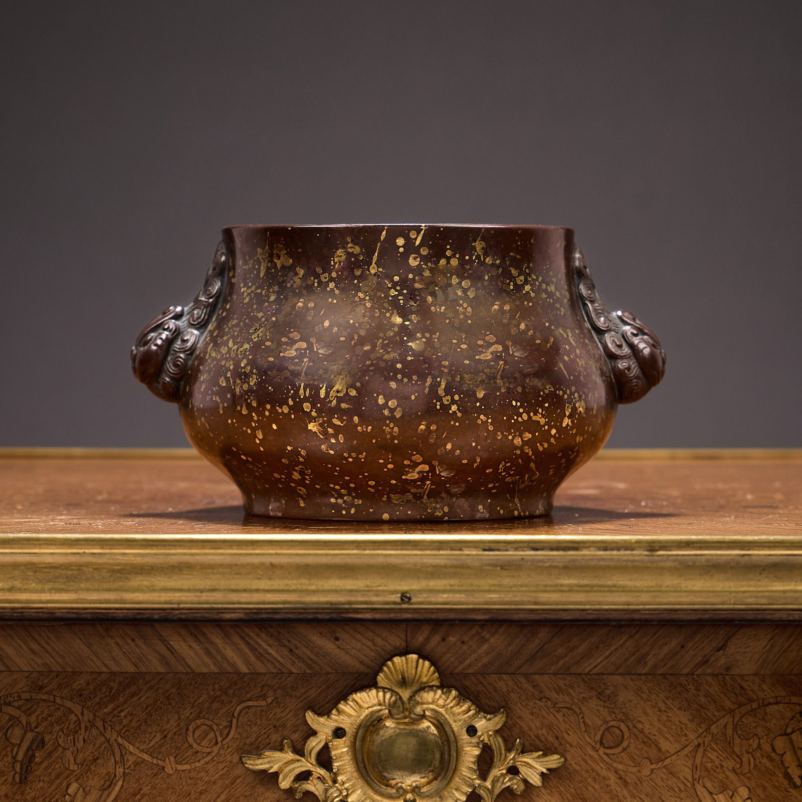 A CHINESE BRONZE CENSER: A CHINESE BRONZE CENSER with lion head style handles, with goldish mottled decoration to surface, marked to underside, 17cm wide x 9cm high