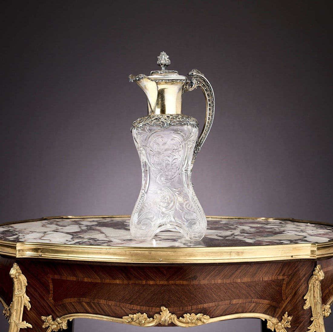 A FINE VICTORIAN SILVER MOUNTED 'ROCK CRYSTAL' STYLE CLARET JUG C. 1900: A FINE VICTORIAN SILVER MOUNTED 'ROCK CRYSTAL' STYLE CLARET JUG C. 1900 the early 20th century wine jug of waisted square form, with floral decorated scroll handle and hinged cover with fruiting finia