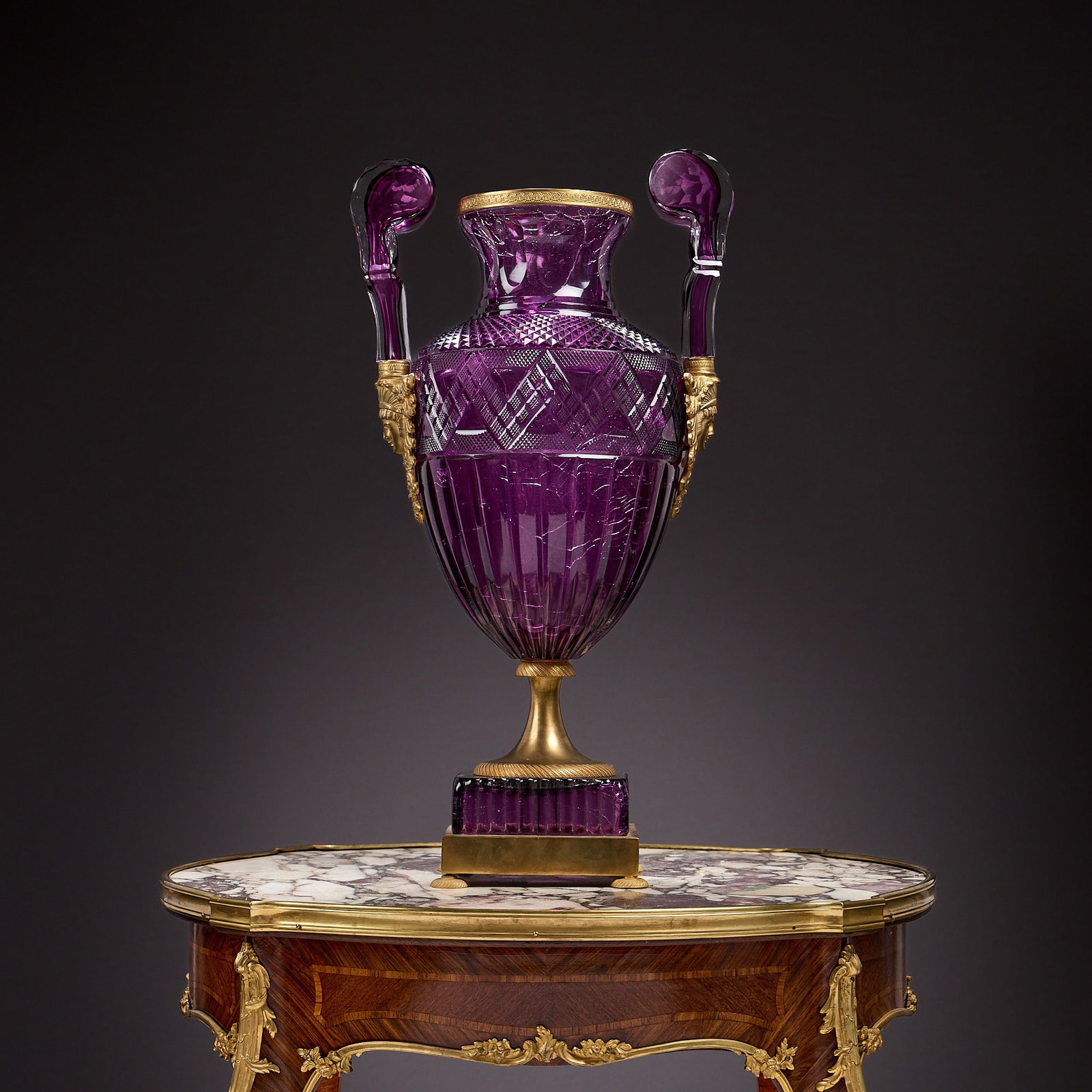 A RUSSIAN AMETHYST COLOURED CUT GLASS AND GILT BRONZE VASE, PROBABLY EARLY 20TH CENTURY: A RUSSIAN AMETHYST COLOURED CUT GLASS AND GILT BRONZE VASE, PROBABLY EARLY 20TH CENTURY the Imperial Russian amphora shaped vase with amethyst tinted cut glass body with a wide band of zigzags and rai
