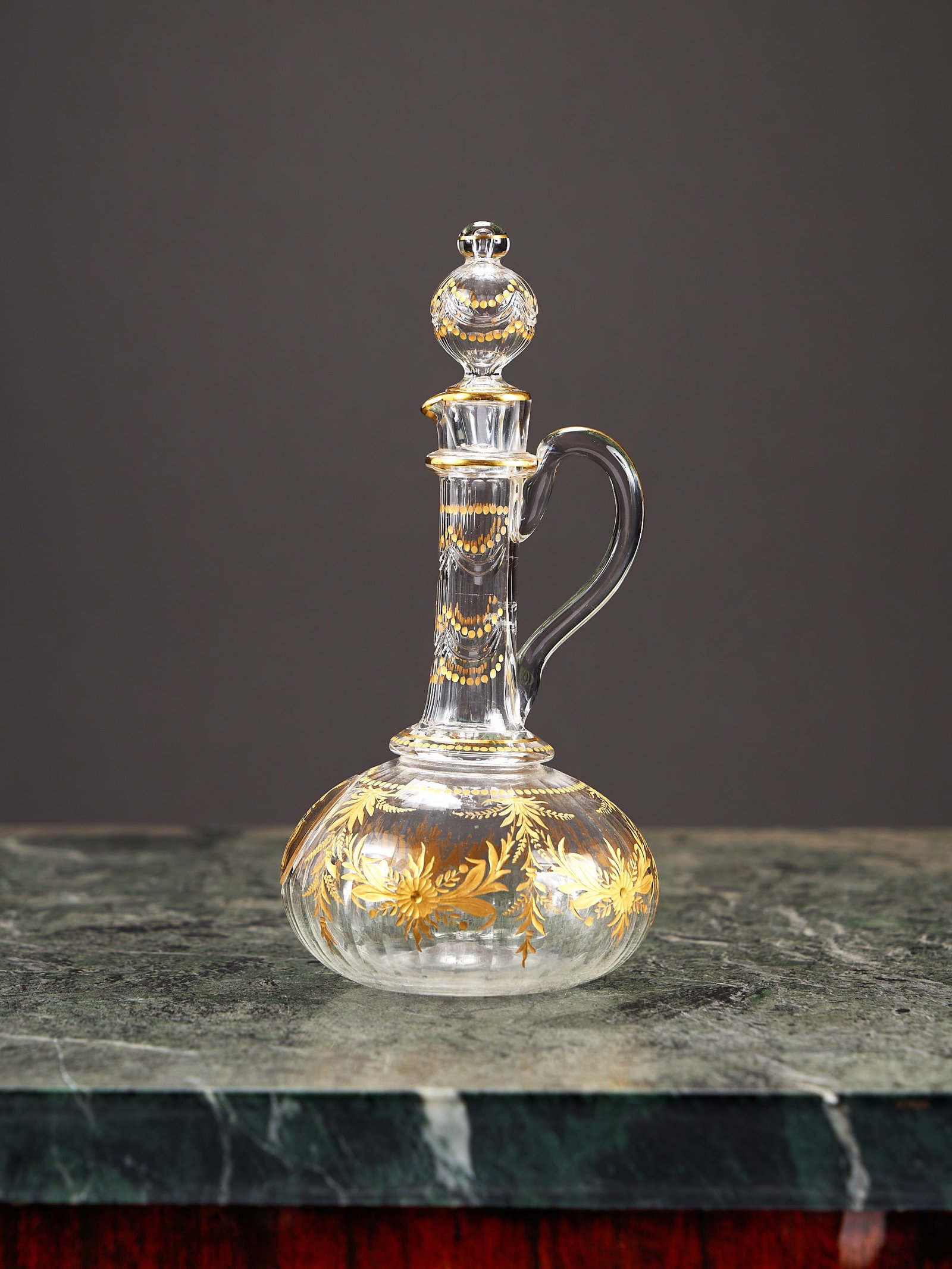 A LATE 19TH / EARLY 20TH CENTURY GILDED GLASS CLARET JUG / DECANTER: A LATE 19TH / EARLY 20TH CENTURY GILDED GLASS CLARET JUG / DECANTER probably French, in the style of St Louis, unmarked, the faceted bulbous body with long faceted neck and scroll handle, with spheric