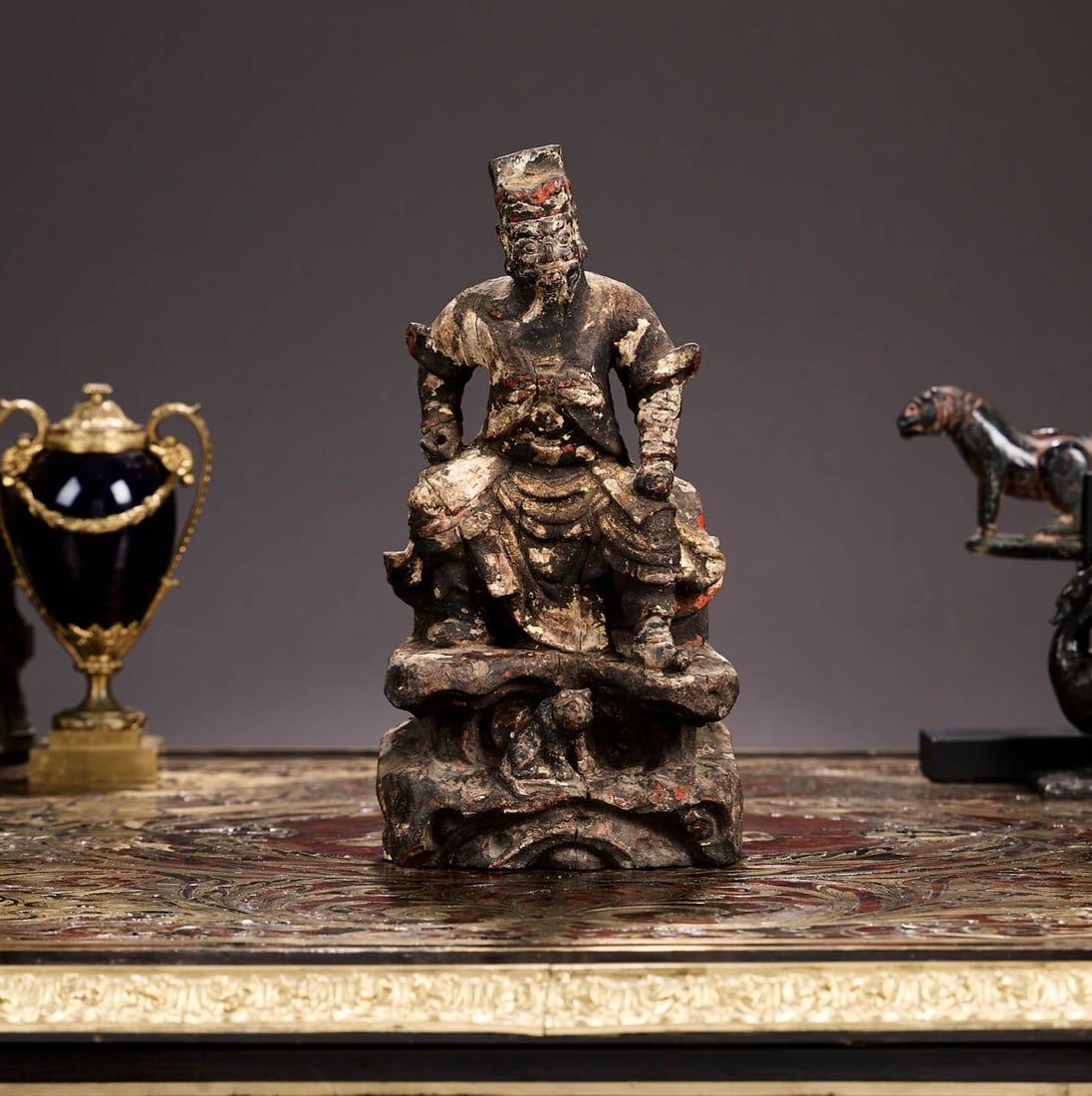 A CHINESE QING DYNASTY CARVED WOOD FIGURE OF A GUARDIAN DEITY: A CHINESE QING DYNASTY CARVED WOOD FIGURE OF A GUARDIAN DEITY probably 18th century, the carved, painted and gilt decorated warrior figure stood on a rocky base with a small beast at his feet, either 