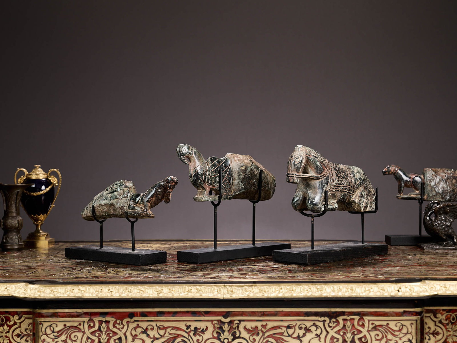 THREE INDIAN 13TH CENTURY STYLE SCHIST CARVED CORBELS: THREE INDIAN 13TH CENTURY STYLE SCHIST CARVED CORBELS modern, carved in green stone, comprising a woman, bird and horse issuing from roughly hewn blocks, mounted on a later stands, the largest 28cm wi