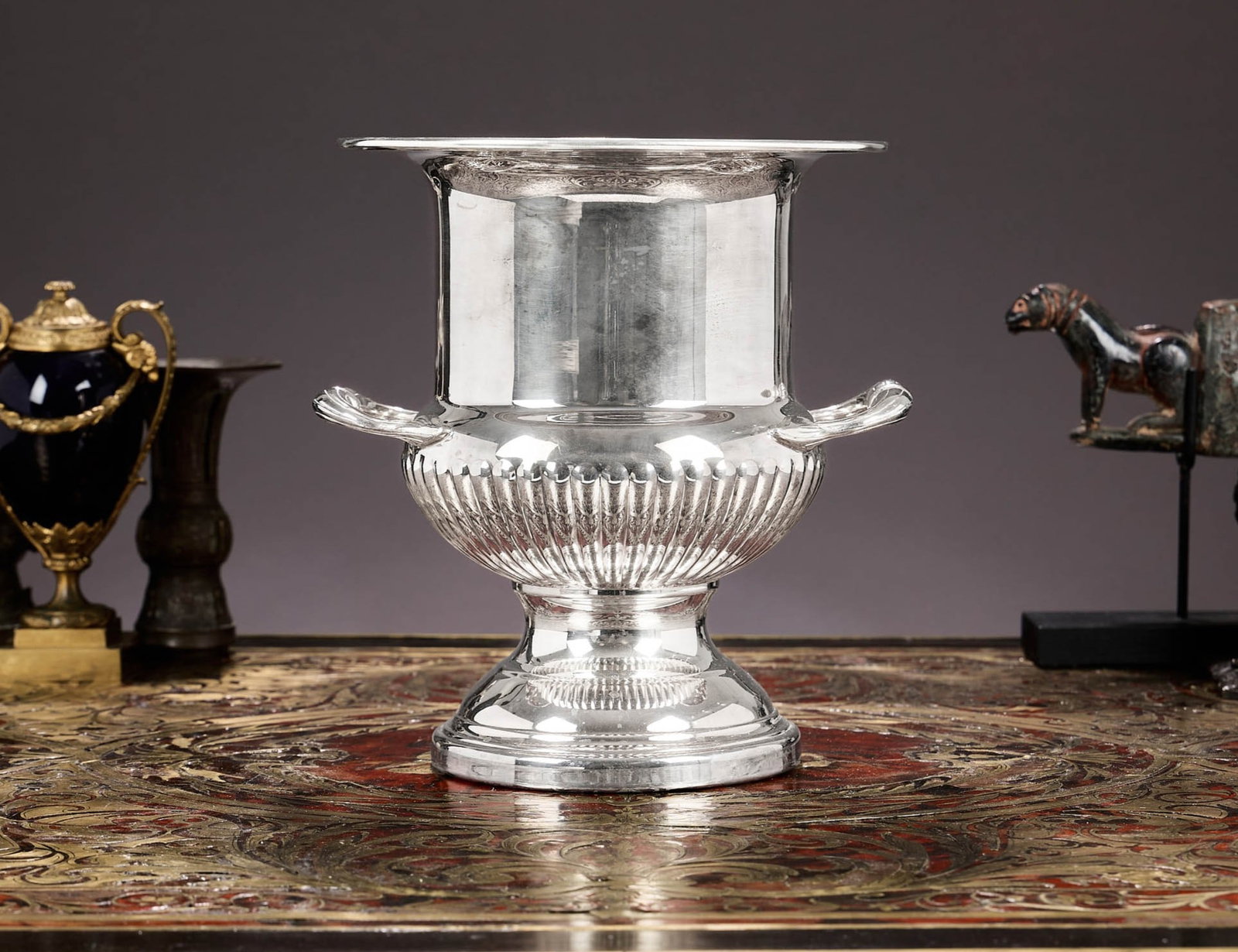 A GEORGE III STYLE SILVER PLATED WINE COOLER: A GEORGE III STYLE SILVER PLATED WINE COOLER or champagne bucket, in the form of a Campana urn, with lobed base and raised on a domed foot, unmarked, 26cm high