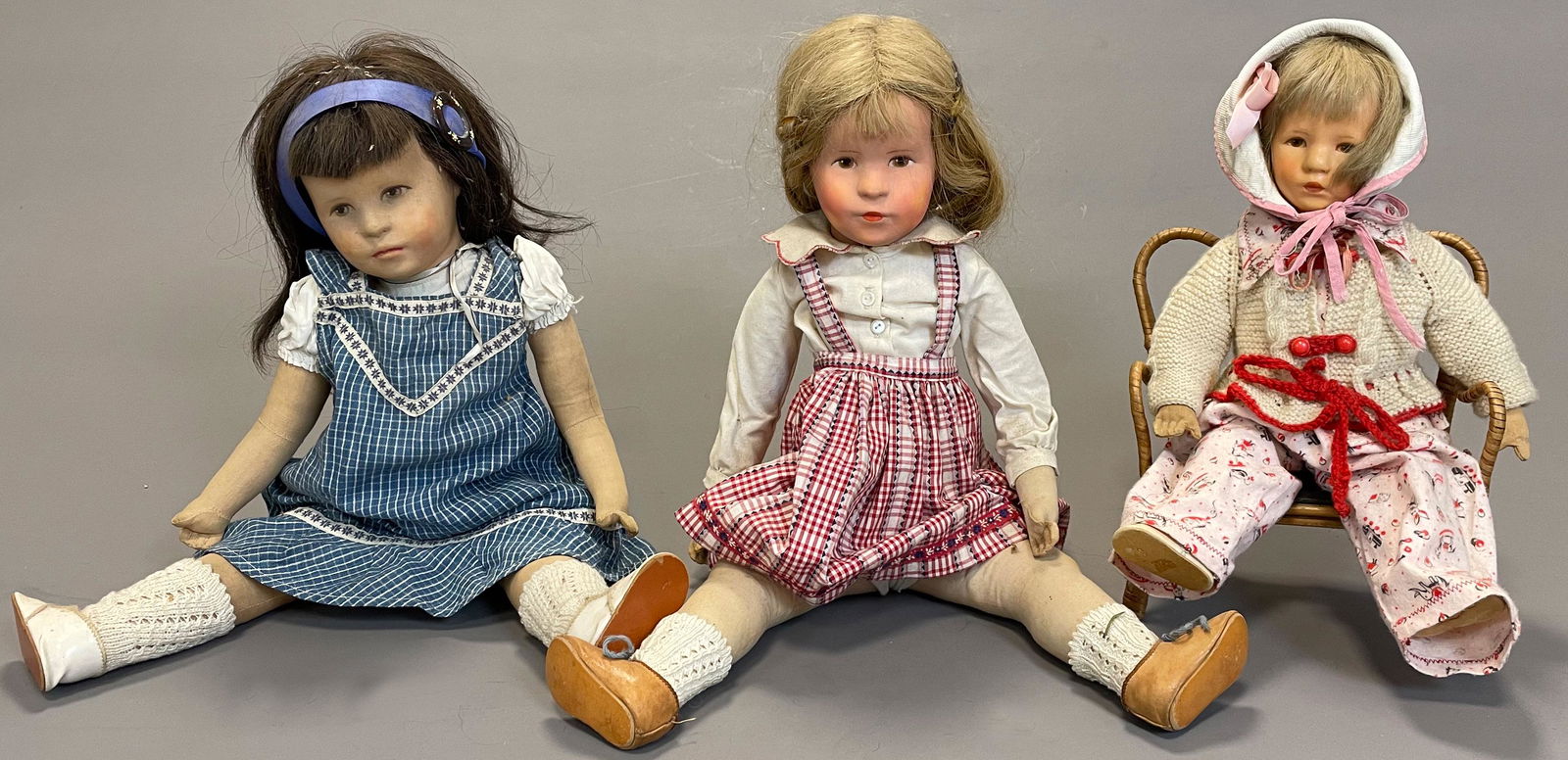 3 KÄTHE KRUSE dolls. Old.: Up to circa 52 cm high. Synthetic-head-dolls. Real hair wigs. One doll sitting on a bench. Old clothes. Played condition. See photos.