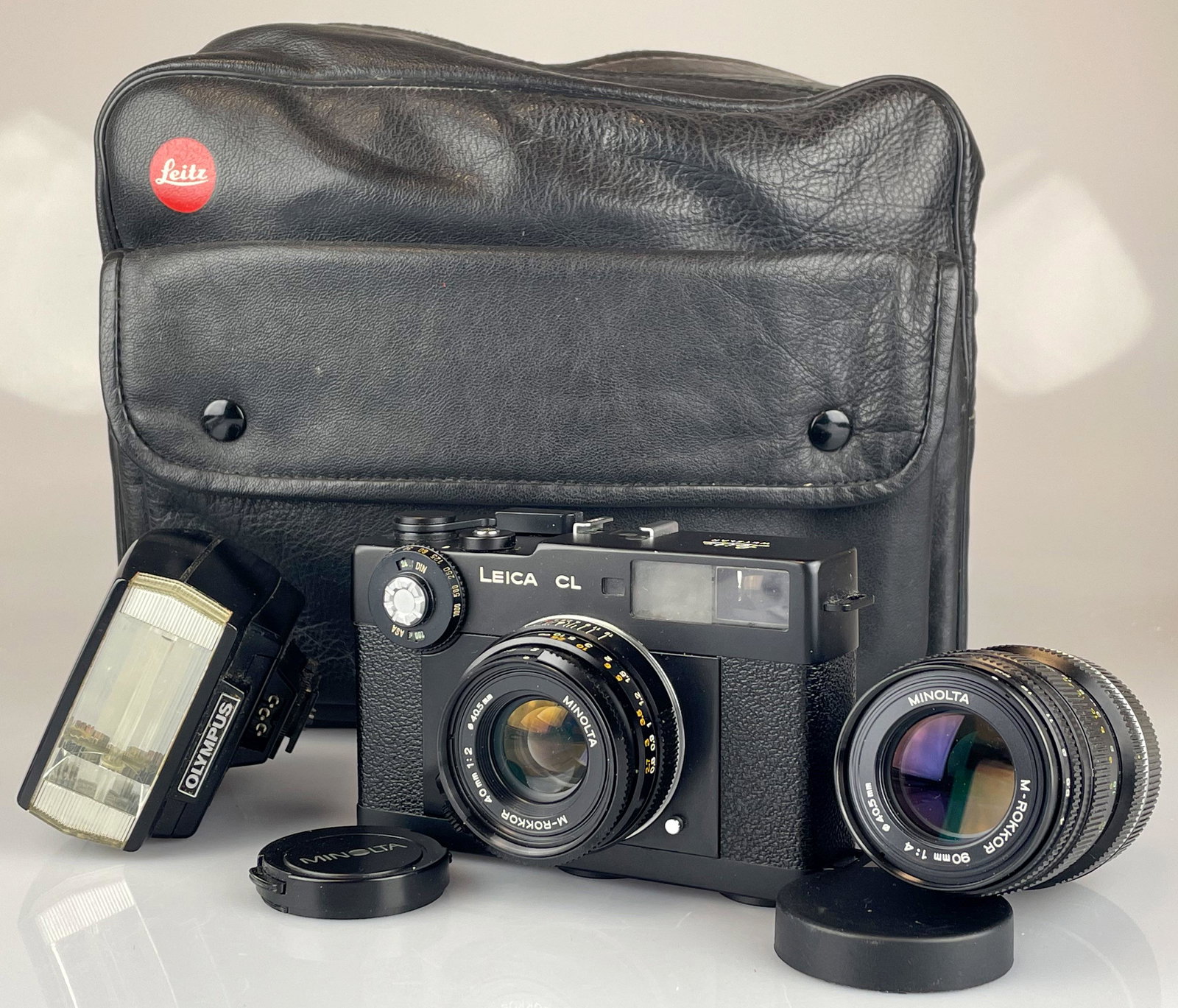 Fotokamera Leica CL. Leica CL photo camera.: Objektiv Minolta M-Rokkor 40 mm 1:2 / 40,5 mm. Nr. 2109648. Dazu 1x Objektiv Minolta M-Rokkor 90 mm 1:4 / 40,5 mm. Nr. 2010635 und 1x Blitzlicht von Olympus "Electronic Flash T20". Mit Tragetasche. Fu
