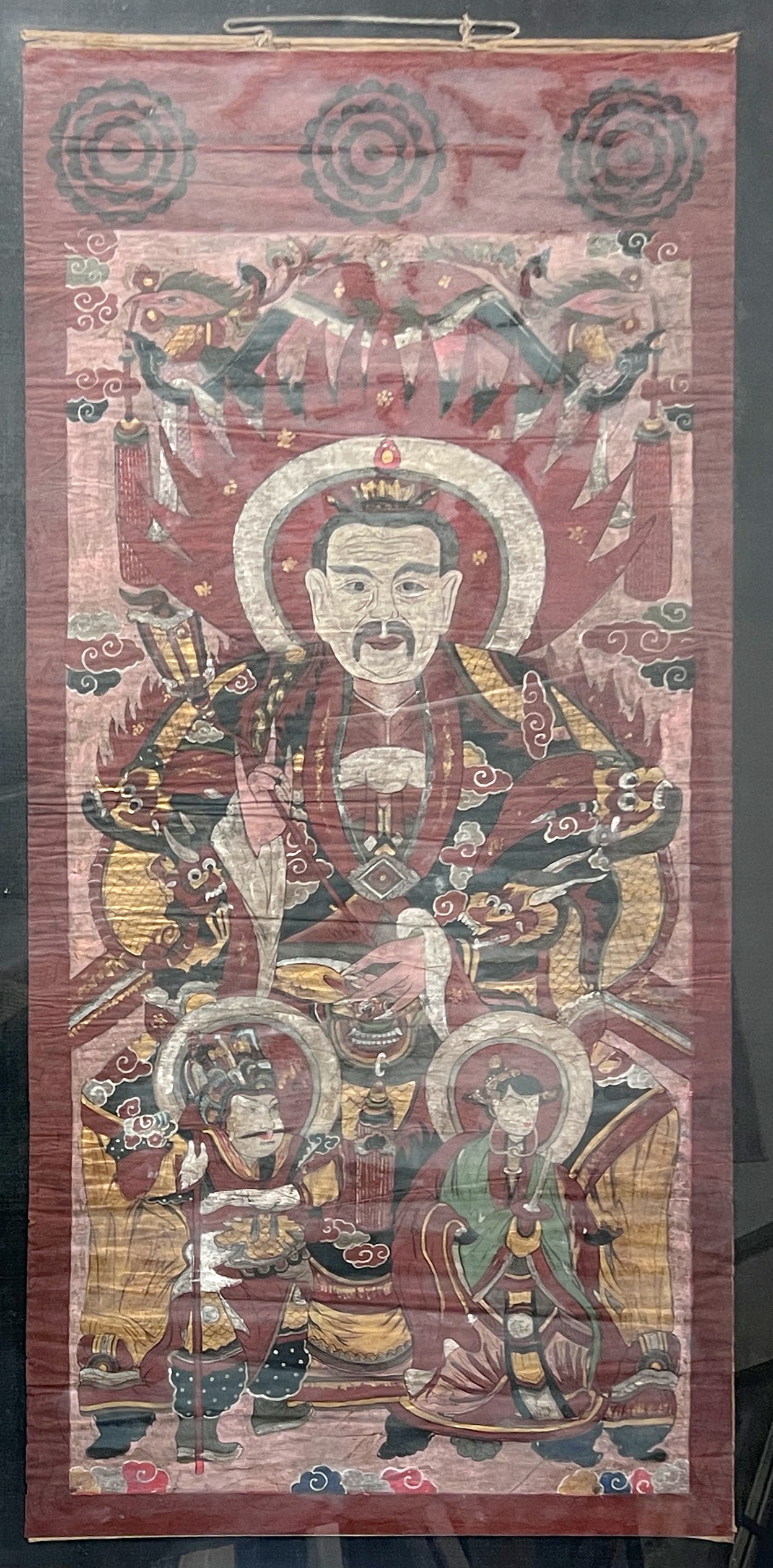 Thangka. "Drei Reinen". China. Um 1900.: Circa 116 cm x 55 cm. Circa 130 cm x 70 cm mit Rahmen. Papier. Thangka. Polychrom bemalt. Darstellung der "Drei Reinen" und Teil des aus drei Bildrollen bestehenden Zyklus der "Drei Reinen". Sie bezei