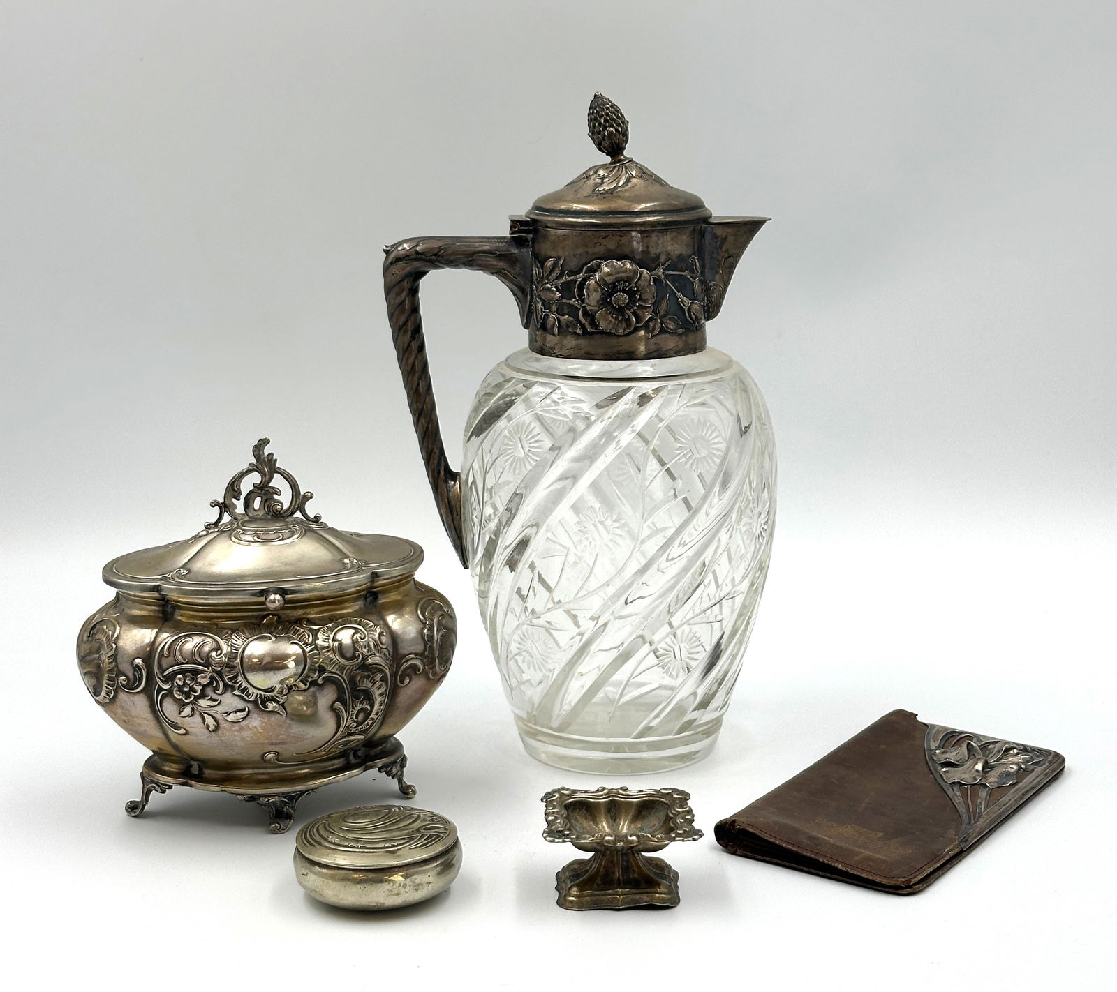 5-teiliges Konvolut Silber. Schenkkanne, Zuckerdose, Pillendose, Salière, Lederetui. 5-piece silver: Approx. 294 grams total weight (without jug and Art Nouveau leather case). Embossed, stylised floral decoration. Approximately 5.5 cm in diameter, the pill box with hinged lid. Embossed, stylised flor