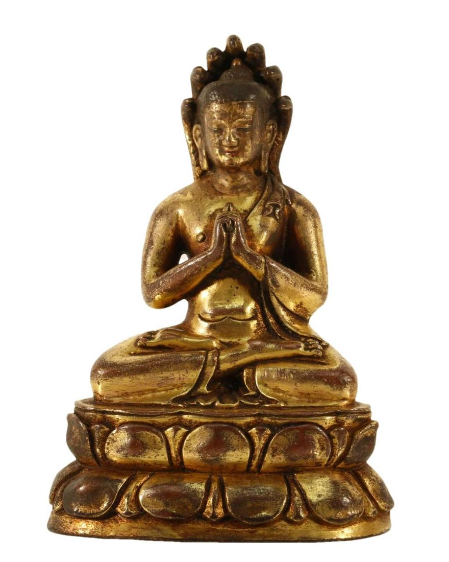 A Gilt-Bronze Figure Of Buddha Shakyamuni: A Gilt-Bronze Figure Of Buddha Shakyamuni. Seated on a base with a peaceful expression, body rendered clad in a robe, the voluminous drapery elegantly cascading in folds, putting two palms together de