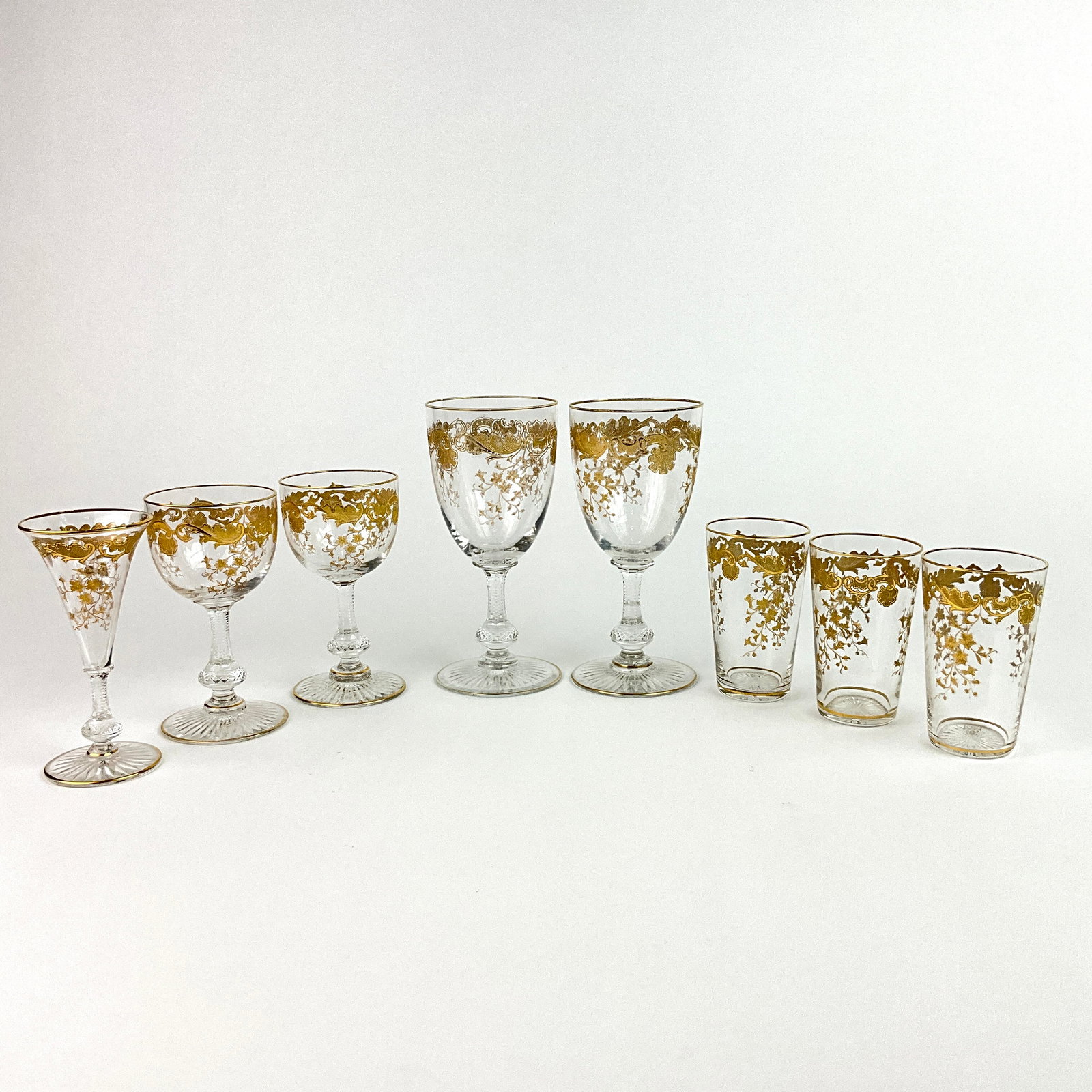Set of 8 Saint Louis Gold Etched Glasses: Gold encrusted folate and floral design to bowls with gilt accents, cut knobbed stem, and a start cut foot except the juice cups.8 Saint Louis Gold etched glasses. one small wine glass, 2 wine glasses