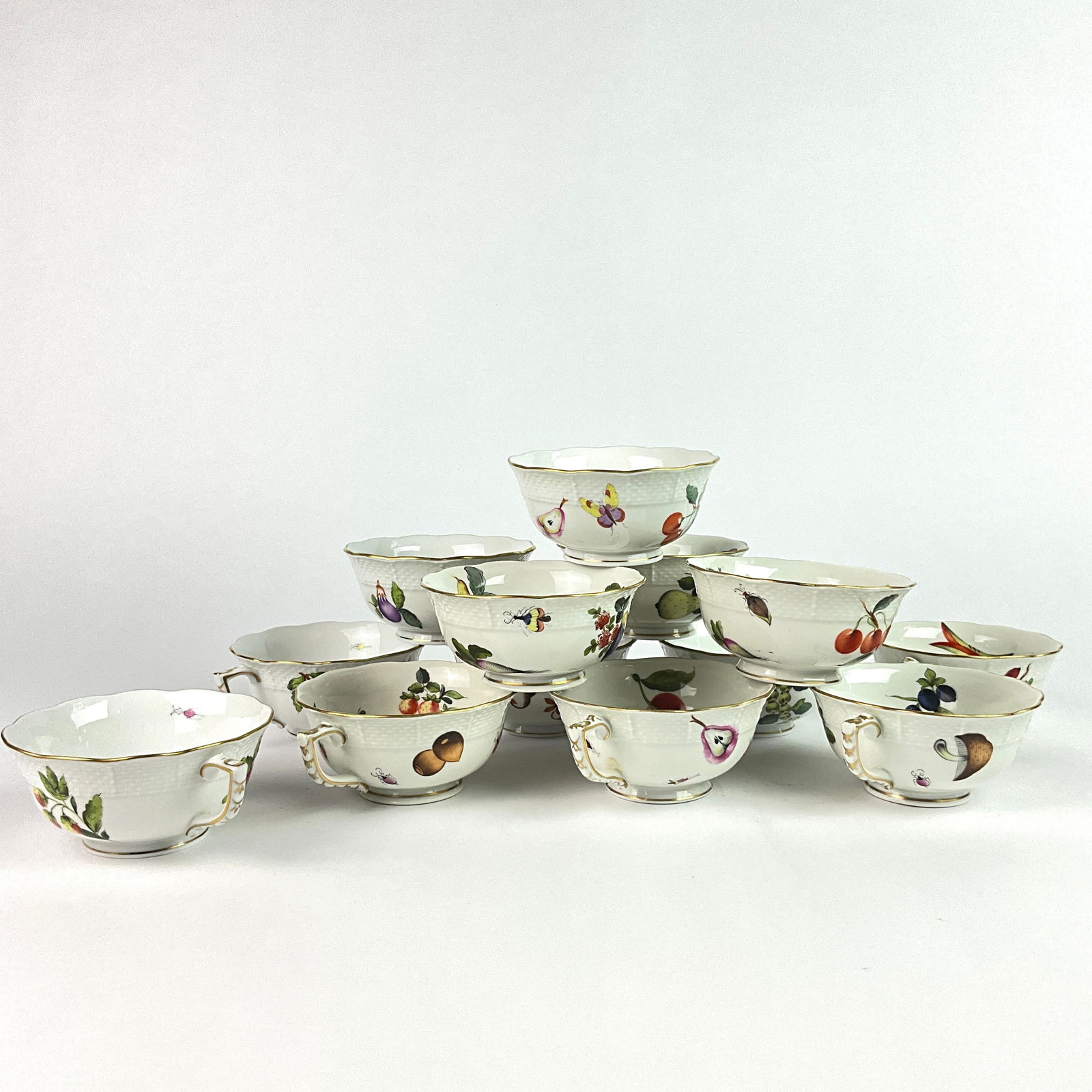 13 Herend Market Garden Tea Cup & Saucers: 12 Saucers, 1 tea cup. Porcelain dinnerware "Market Garden" pattern, hand-painted motifs of various fruits, vegetables and insects front and back. 24 Karat Gold Edges. 5.25" diameter on saucers. 4" di