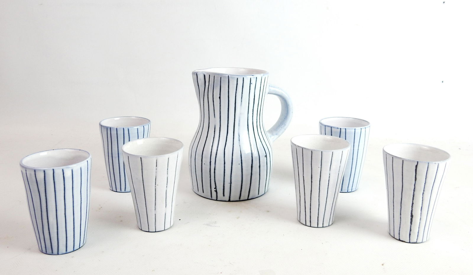 INNOCENTI: Jacques INNOCENTI (1926-1958): Service Ã orangeade comprenant un pichet et 6 verres en cÃ©ramique Ã©maillÃ©e blanc incisÃ©. Signature sur le pichet. (petits accidents sur le pichet).