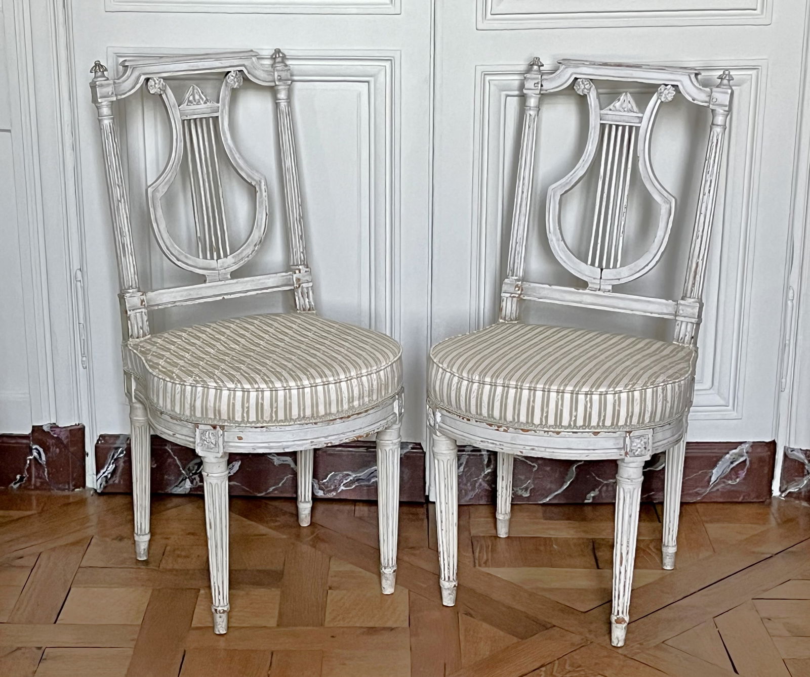 PAIRE de CHAISES en hetre moulure, sculpte et laque creme a dossier ajoure a decor de lyre, reposant: PAIRE de CHAISES en hetre moulure, sculpte et laque creme a dossier ajoure a decor de lyre, reposant sur quatre pieds canneles. Des de raccordement a decor de fleurettes. Estampille de David. Epoque L
