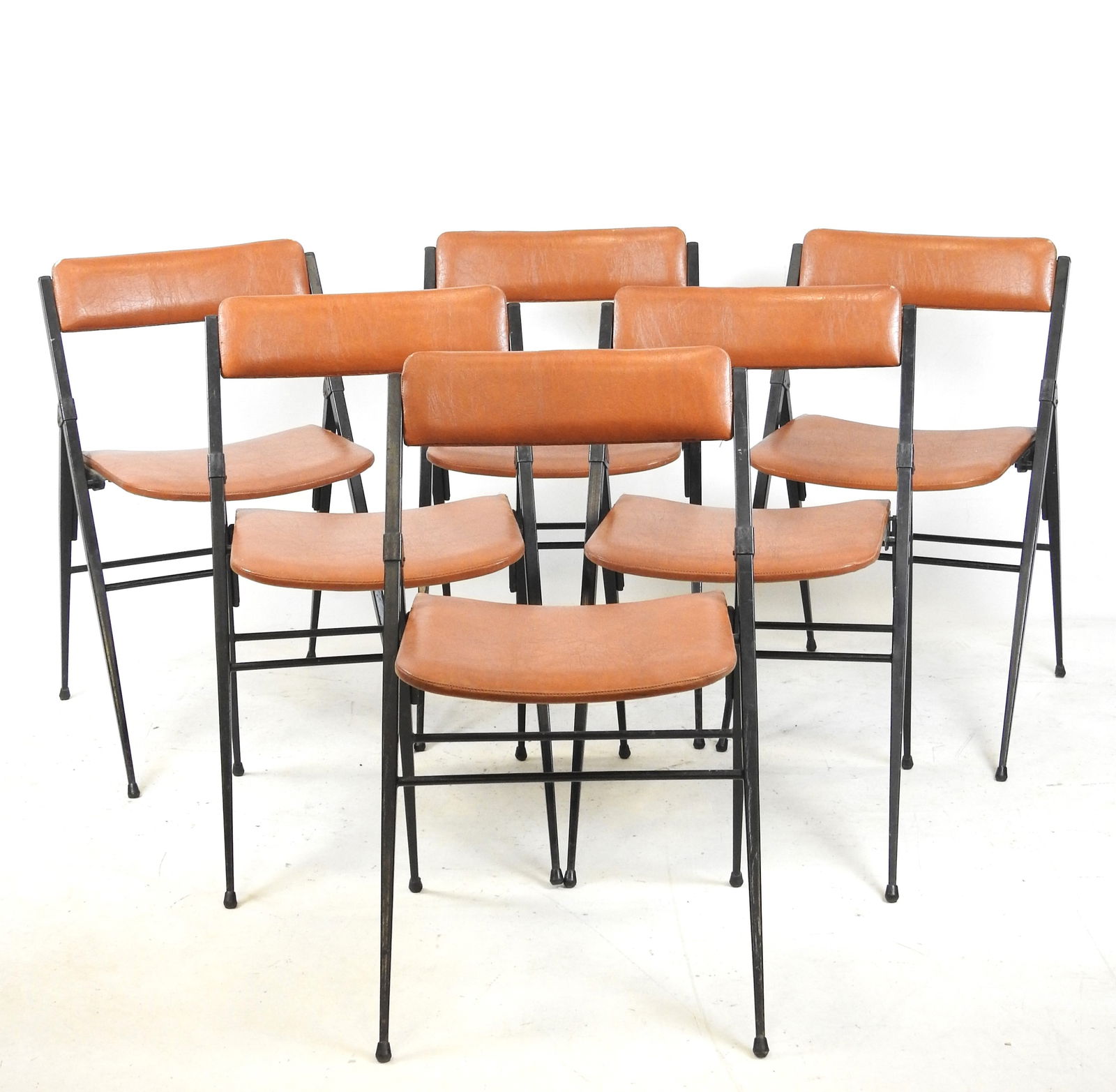 SIX CHAISES PLIANTES pieds compas en fer forge , dossier et assise en skai marron. Annees 1960.: SIX CHAISES PLIANTES pieds compas en fer forge , dossier et assise en skai marron. Annees 1960. Ancienne etiquette MAT sous l'assise. H. 79 - L. 47 - P. 45 cm. Legeres usures aux assises.