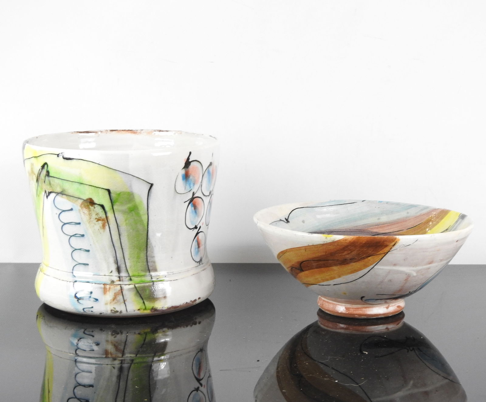 David MILLER (1942 - 2008) : Cache pot circulaire: David MILLER (1942 - 2008) : Cache pot circulaire et une coupe sur pied de forme evasee en ceramique a decor abstrait pour l un et de fruits stylises pour l autre. H. 20 et 11.5 cm - Diam. 23.5 et 25.