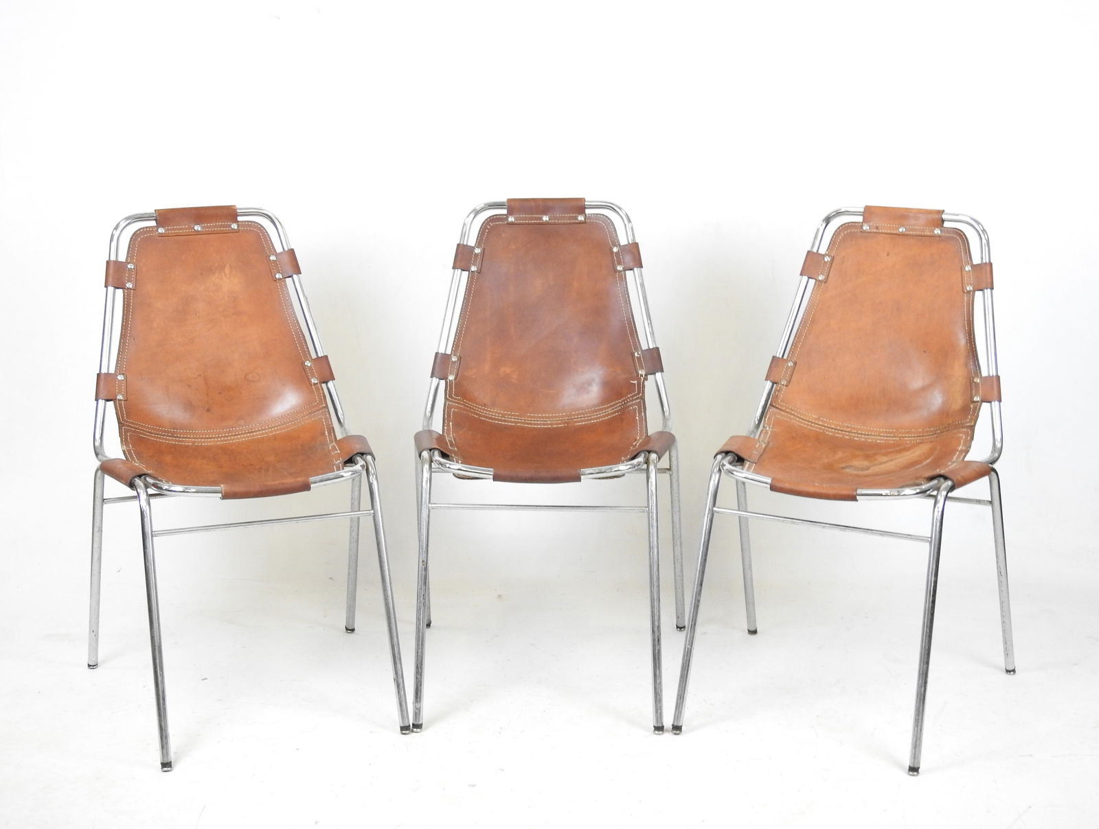 Charlotte PERRIAND (Modele selectionne par) et DAL: Charlotte PERRIAND (Modele selectionne par) et DAL VERA (Editeur)Les Arcs, le modele cree vers 1970Trois chaises a structure en acier tubulaire chrome, cuir havane patine tendu (par languettes de cuir