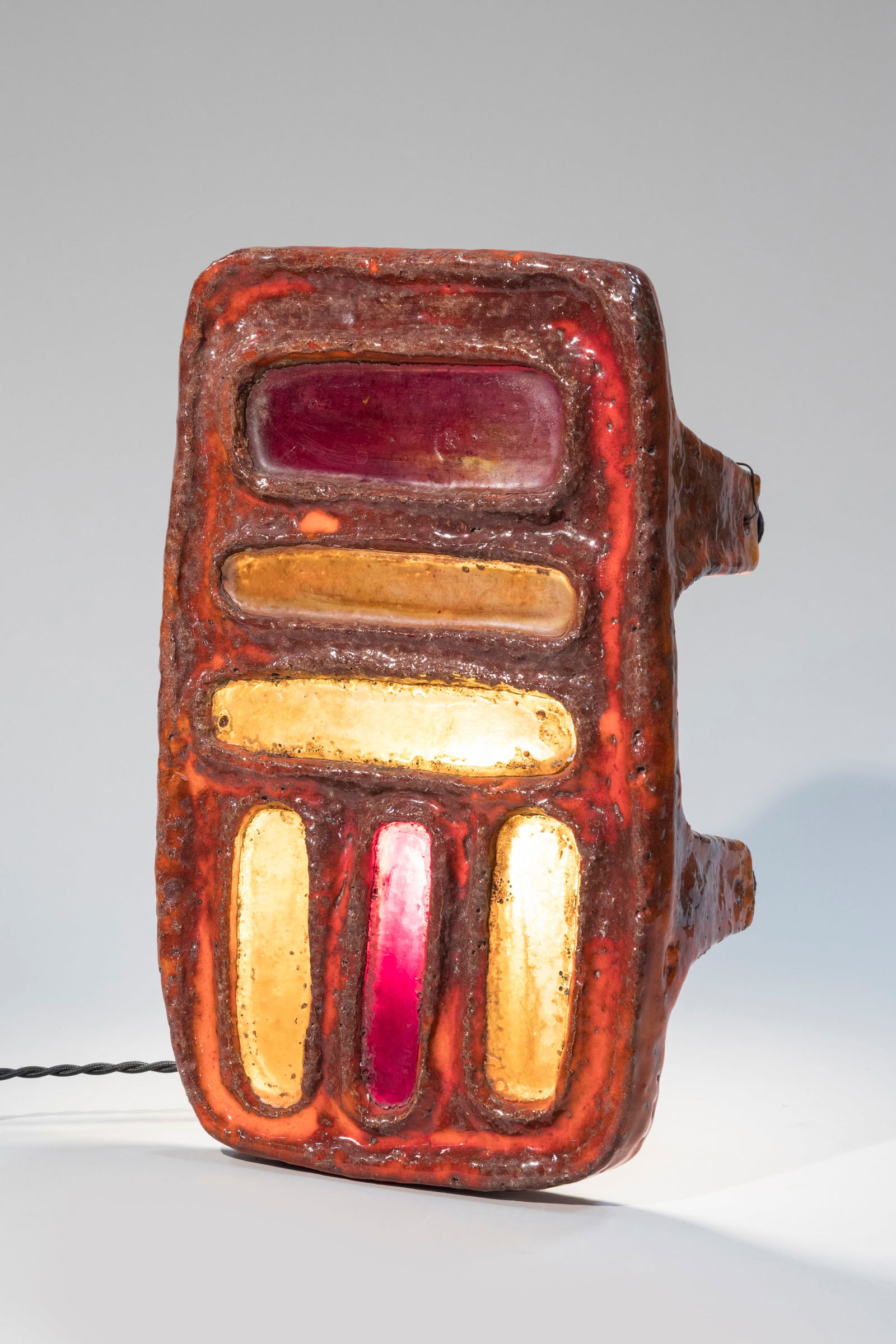 Juliette DEREL (1918-2007) Lampe veilleuse de form: Juliette DEREL (1918-2007)Lampe veilleuse de forme rectangulaire arrondie reposant sur quatre pieds en terre chamottee a couverte orange. Partie centrale agrementee de six plaques en resine refractair