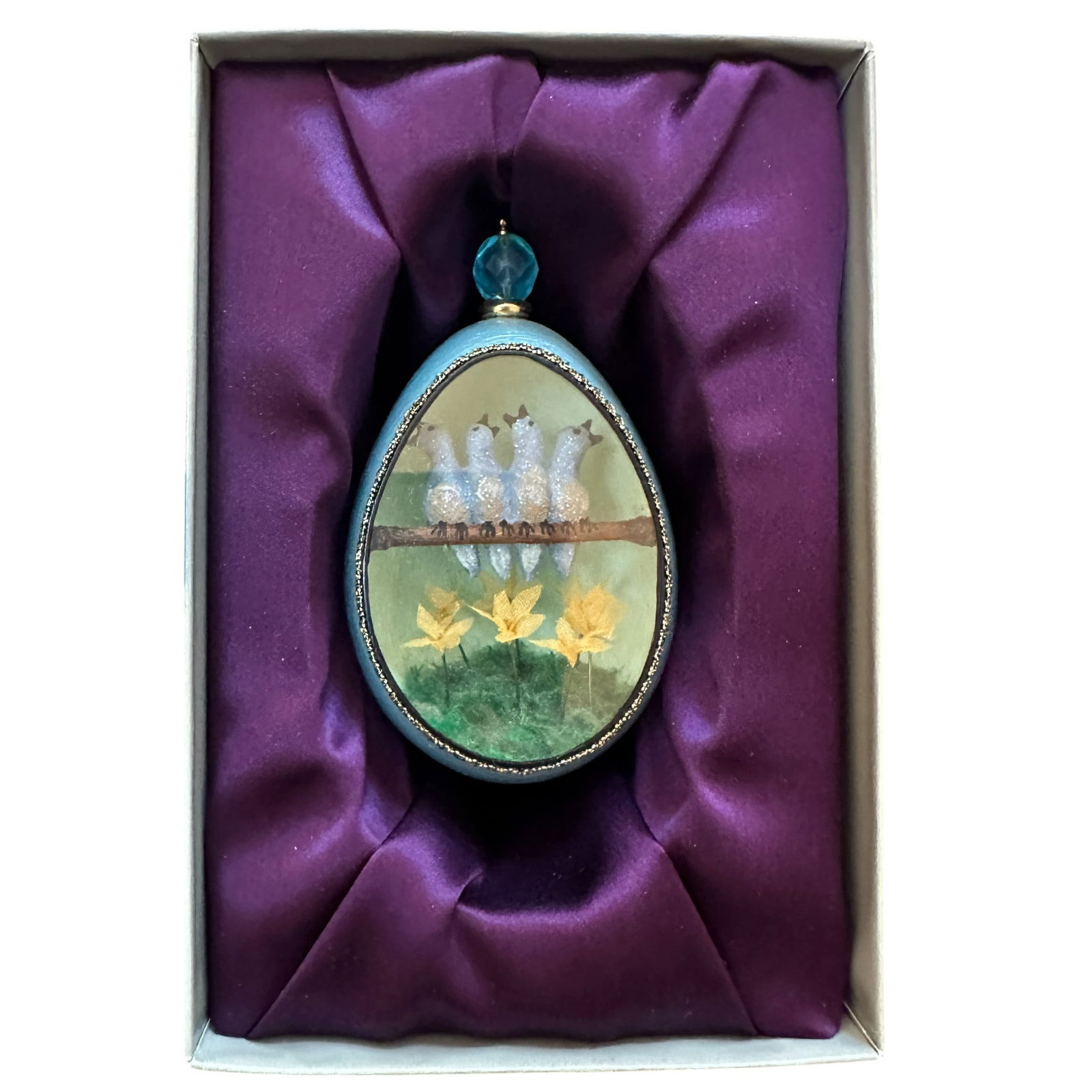 JBW Studios Collectible Four Calling Birds Decorative Egg: The egg has a pale blue exterior with a gold-trimmed oval viewing window revealing a charming interior scene. Inside, four glittering blue birds sit together on a brown branch, each with detailed beak