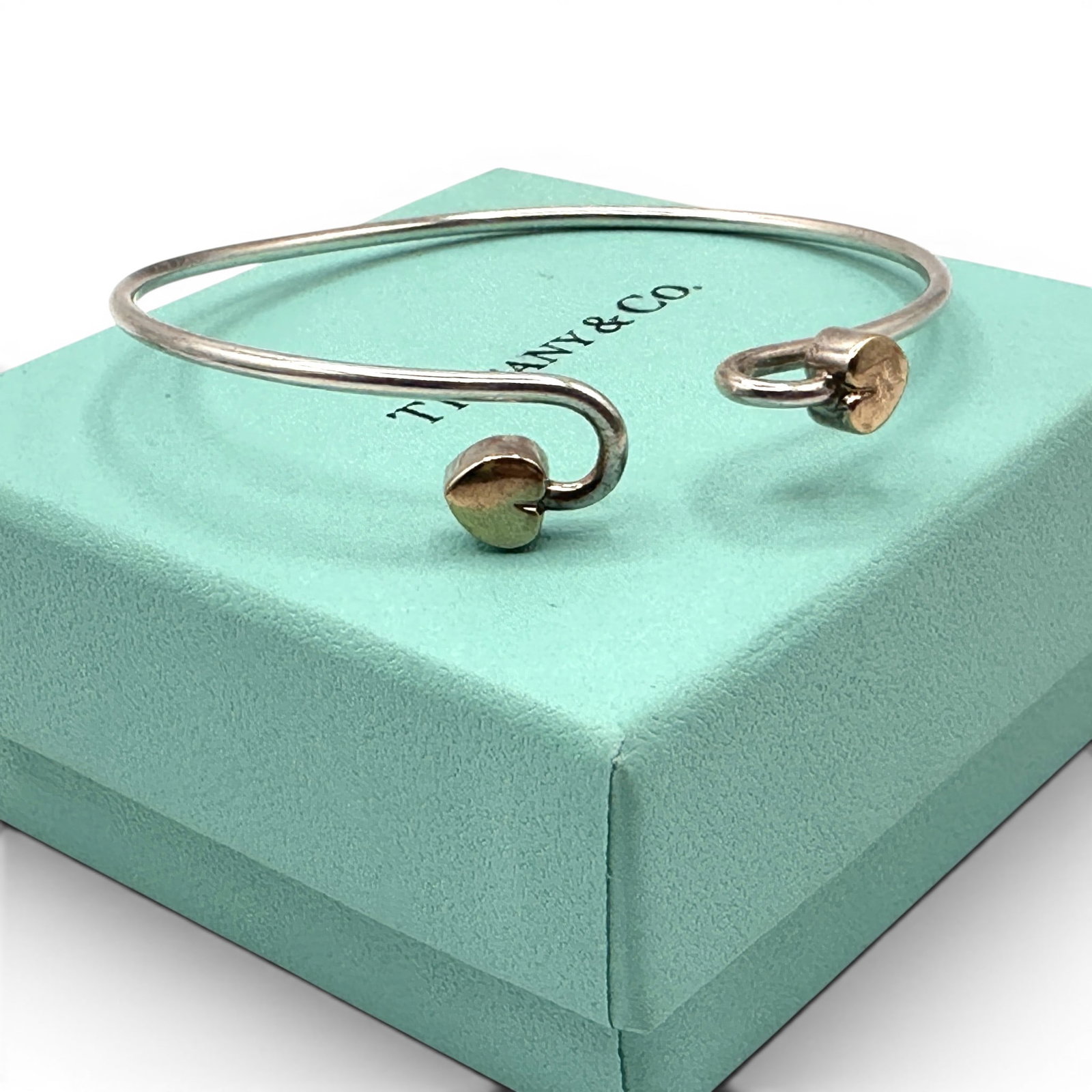 Tiffany & Co. Sterling Silver & 18K Gold Heart Hook Bangle Bracelet: A timeless and elegant Tiffany & Co. sterling silver and 18K gold bangle bracelet, showcasing the celebrated minimalist aesthetic for which the iconic American jeweler is renowned. The bracelet featur