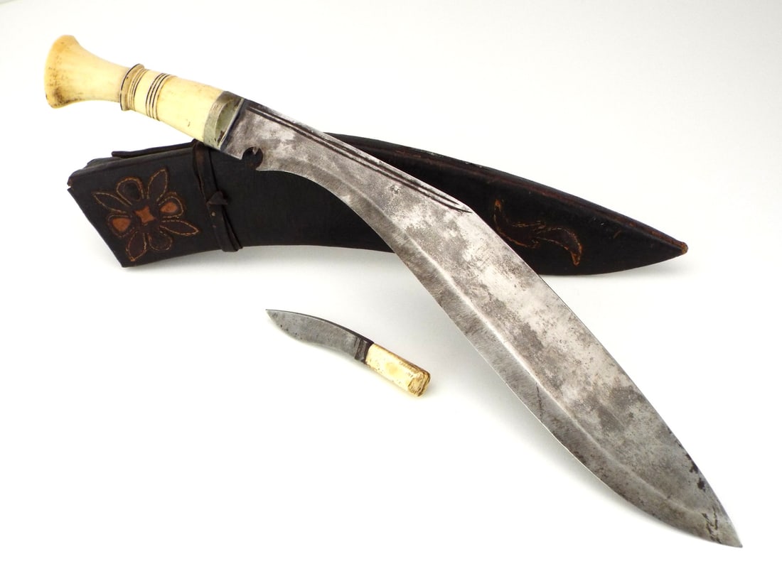Antique Nepalese KUKRI Knife VERY FINE Hilt: Antique Nepalese kukri knife with a steel blade displaying greyish patina and maintaining a sharp edge. Attractive decorated FINE grip showing minor mellowing. Contained in a leather scabbard bearing