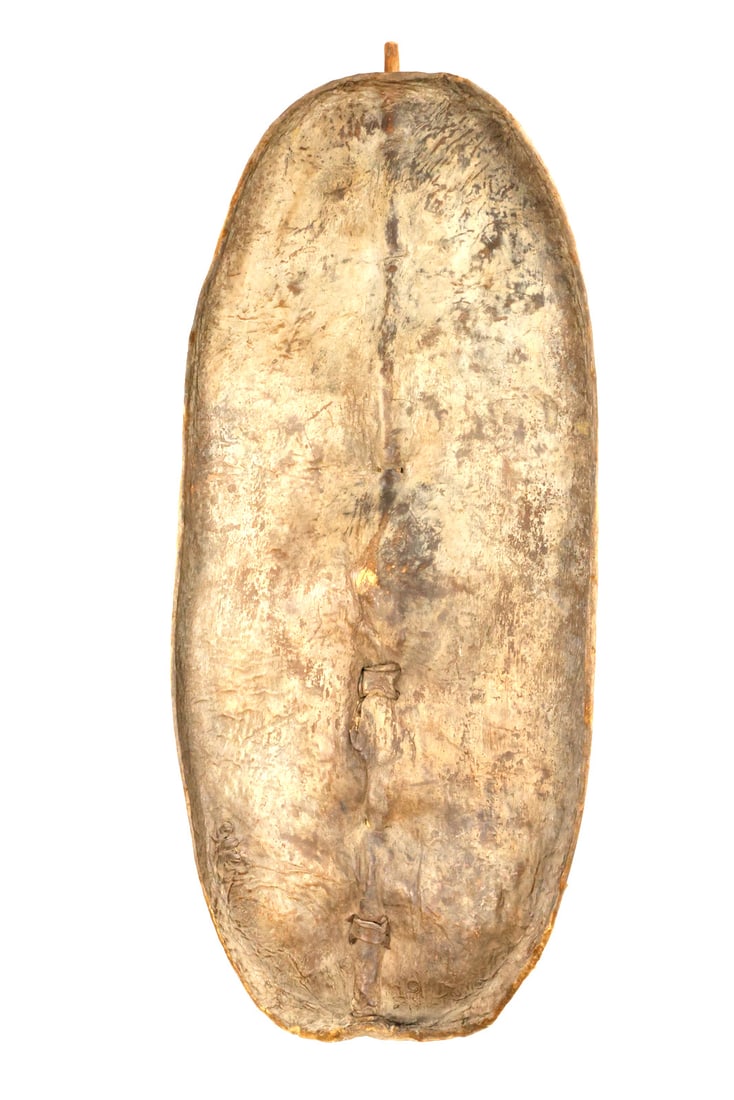HUGE Antique North African Tribal Battle Shield: North African tribal battle shield with an elongated oval form of large proportions crafted from thick hide under mellowed surface. The central wooden spine reinforced by rawhide stitching and looped