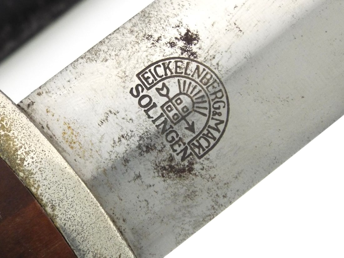 Early German WWII NSKK Dagger EICKELBERG & MACK SOLINGEN: Service blade exhibits a bold "Alles fur Deutschland" engraved translating to "All for Germany" amidst mild oxidation. The contoured walnut grip remains solid, housing a vivid silvered eagle and ename