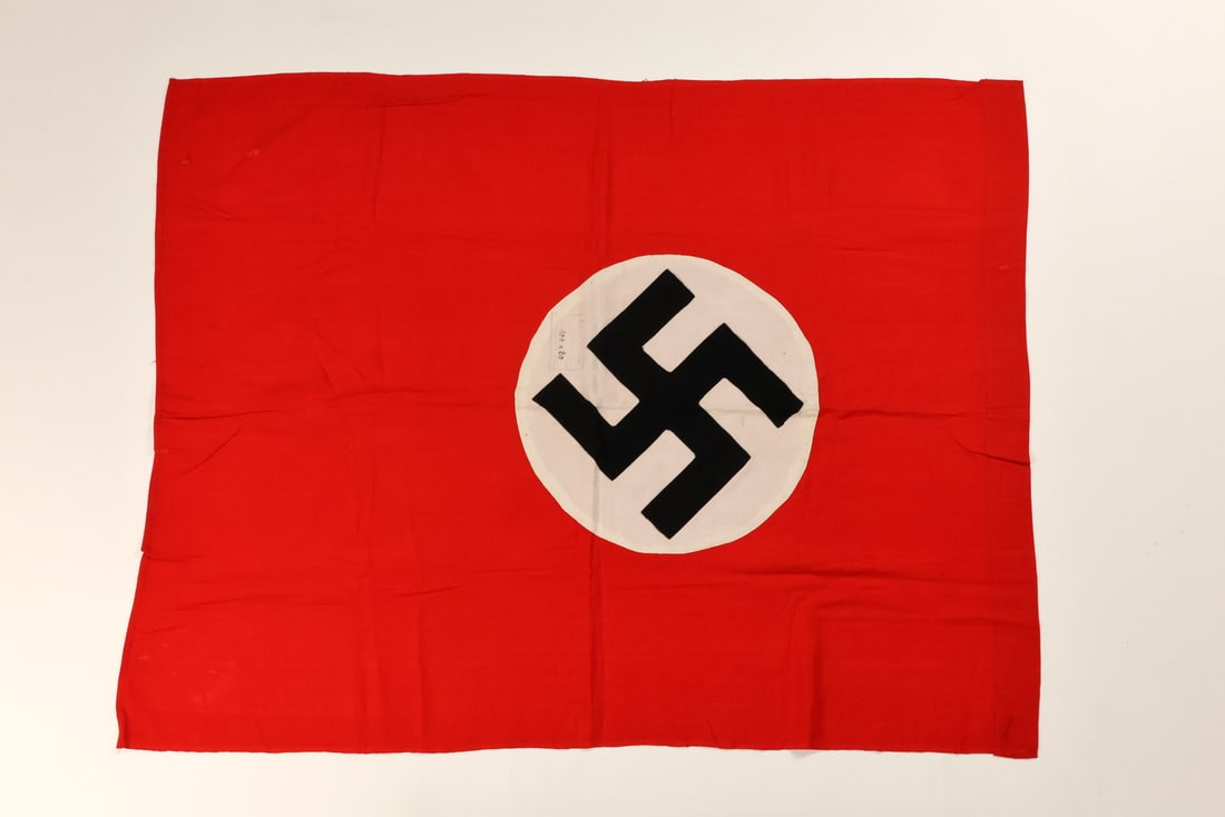 German WWII NSDAP Flag Multi Piece Construction in Cotton: Textile displays a vibrant scarlet field composed of a coarse weave cotton bunting, featuring a central white roundel with an inset black ensign of multi piece construction. Superior stitching defines