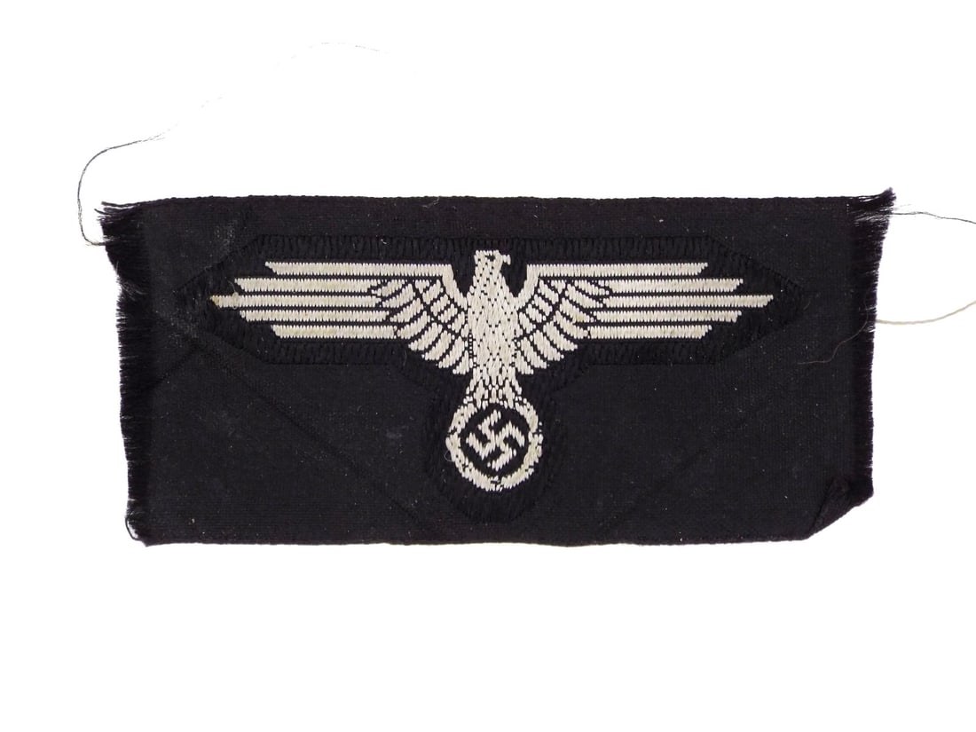 German WWII WAFFEN SS PATTERN INSIGNIA Bevo Machine Woven Silk Thread: Flat wire construction displays an eagle with outspread wings perched above a wreathed ensign, rendered in silver grey rayon thread against a dense black field. The textile body exhibits light field w
