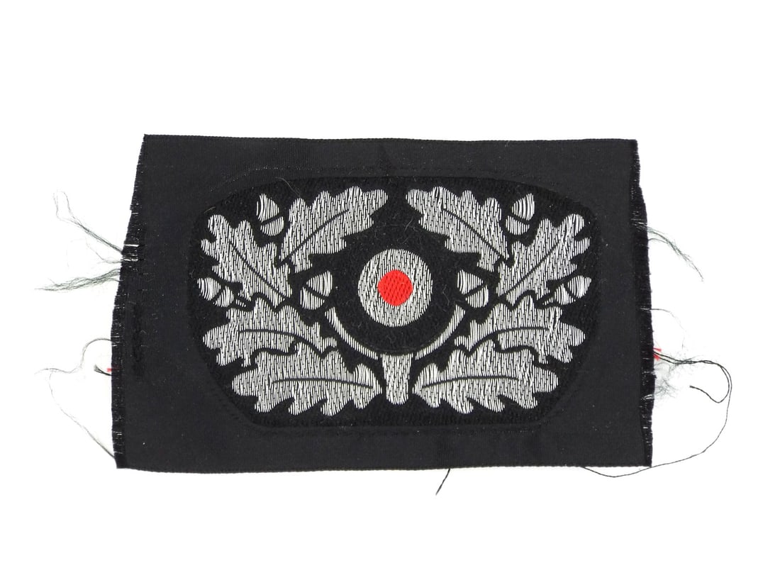 German WWII PANZER BERET INSIGNIA Silver Bullion Oak Leaves: Machine woven textile body displays a muted silver grey thread composition depicting a traditional oak leaf wreath and central acorns, exhibiting minor fraying along the unfinished edges. The tricolor