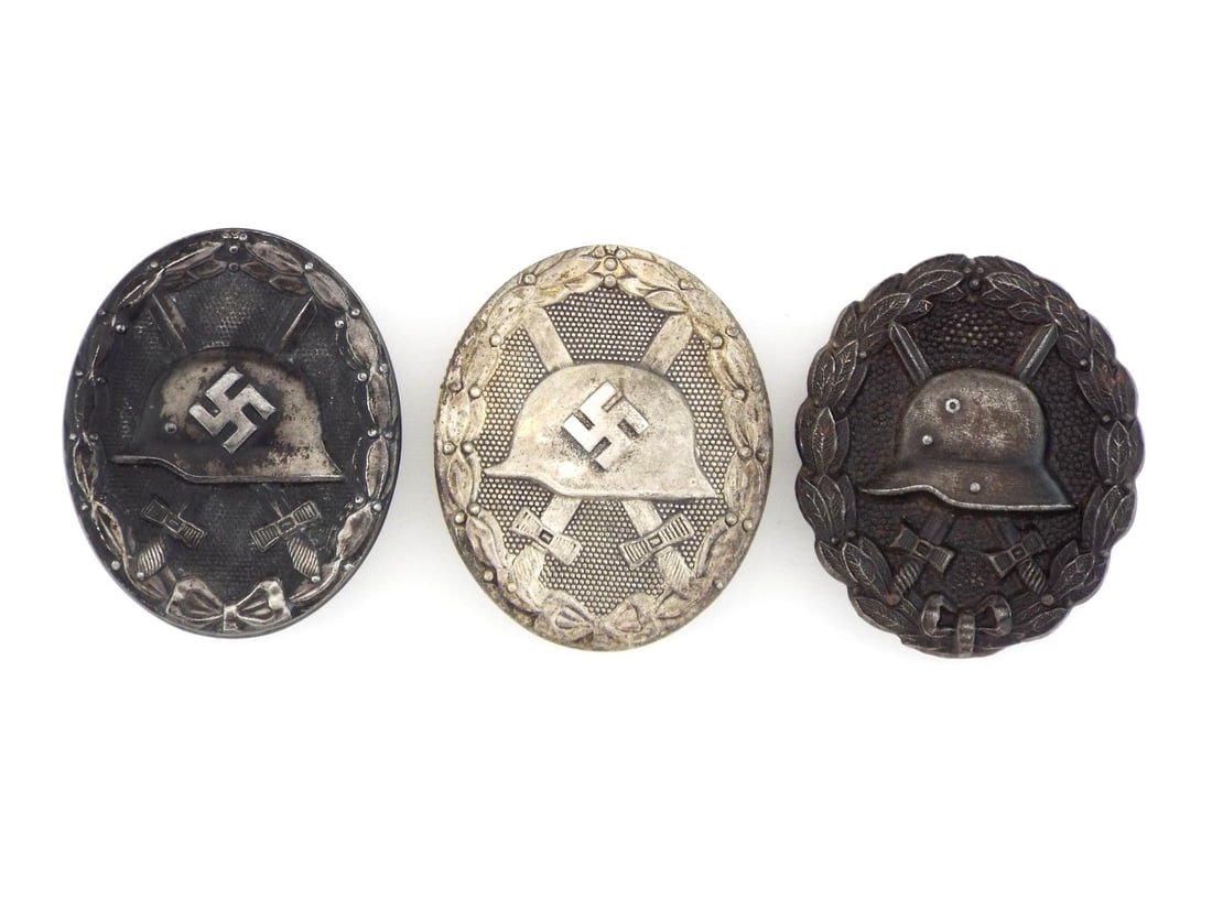 German WWII Wound Badges Black and Silver Grade: Trio comprises one WWI pattern and two 1939 types, 2nd Class silver shows solid construction with maker mark 65 and light tarnish, while 3rd Class black and WWI examples exhibit hollow stamped steel w