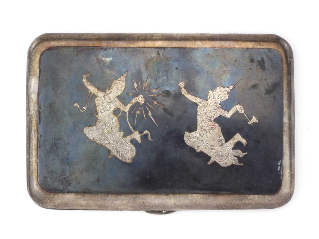 Thai Early Century SILVER CIGARETTE CASE Inlay Work: Silver body displays tarnish and surface abrasions consistent with frequent handling. High relief inlay on the lid depicts Mekhala and Ramasun with minor oxidation to the black alloy. Retaining strap