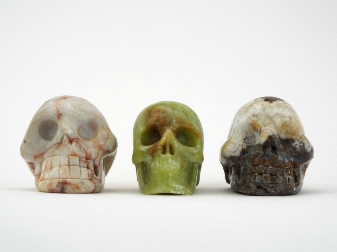 Curio Lot SKULL TRIO Hand Carved Serpentine & Jasper: Trio of memento mori zoomorphic carvings comprising a pale lime serpentine piece, a ferruginous veined marble example and an agate skull. No structural defects or significant chips noted to the craniu