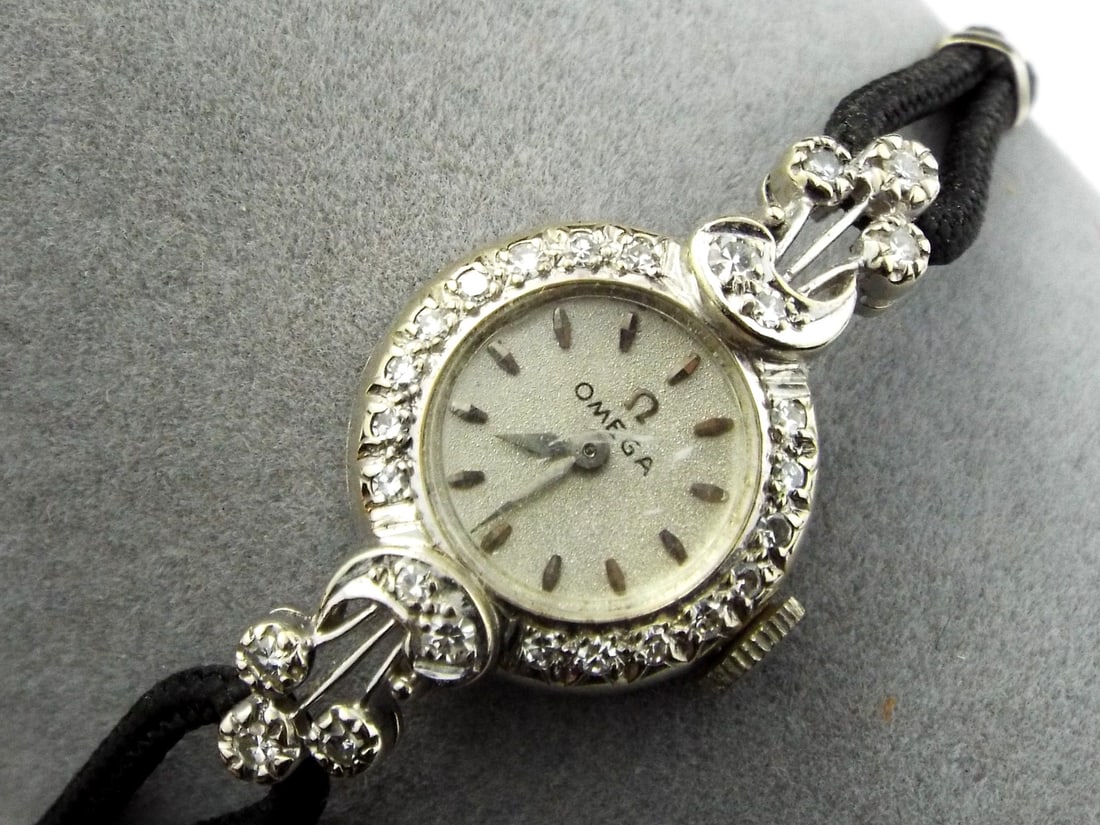 Swiss Mid Century OMEGA 14K White Gold & Diamond Cocktail Watch: Petite circular 14K white gold case displays expected micro scratching, featuring a silvered sunburst dial with applied baton markers and centered Omega logo showing light patina throughout. The bezel