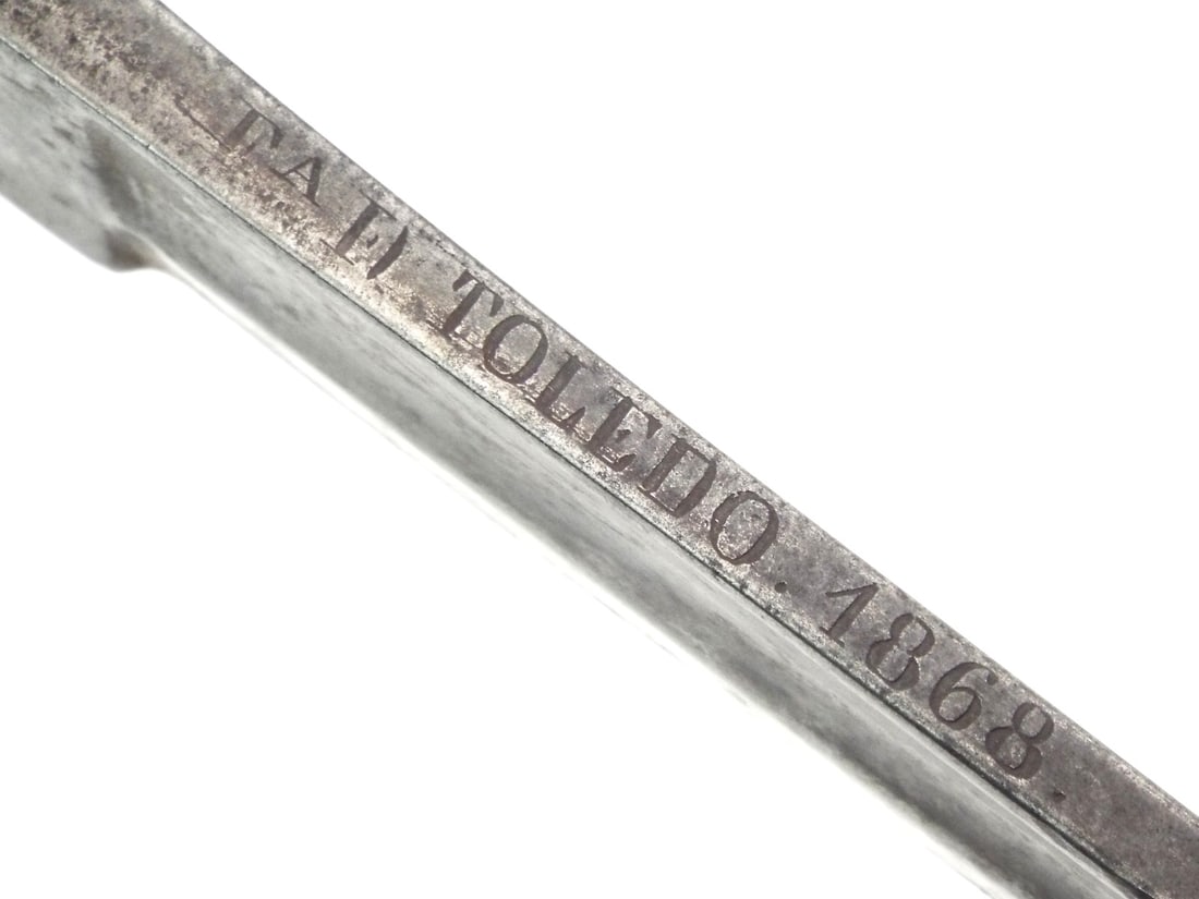 Spanish 1868 Glorious Revolution CAVALRY SWORD TOLEDO Made: Heavily patinated blade featuring a single wide fuller and clear spine inscription reading FA. D. TOLEDO 1868 for the Toledo Weapons Factory. Half basket iron guard displays a crown over PV stamp. Sha