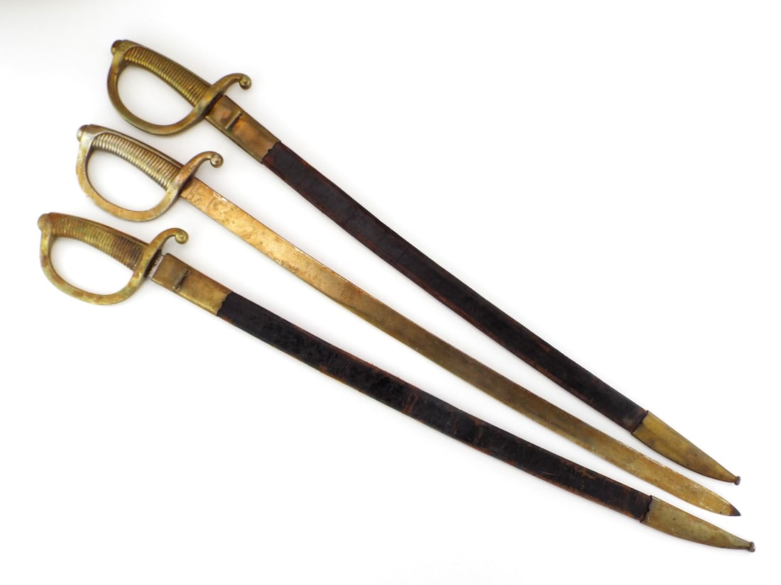 Group of Three Spanish 19th C. ARTILLERY BRIQUET SWORDS: Group of three Spanish Model 1840 artillery briquet swords, featuring ribbed brass D-guard hilts and single edged steel blades inscribed ART FAB DE TOLEDO with dates 1874 and 1897, two housed in leath