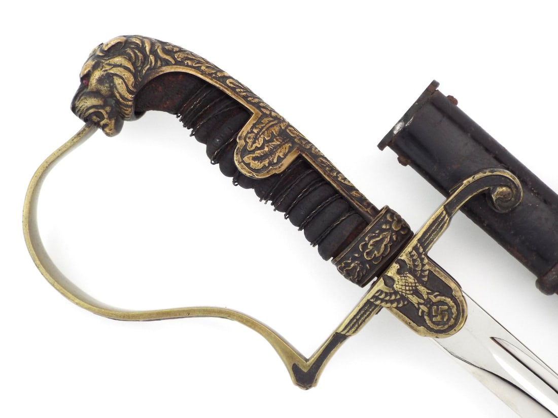 German WWII Army Officer Sword Lion Head Pommel with Ruby Eyes: Steel blade presents a deep fuller and brilliant luster, displaying minimal age toning. The brass hilt features a highly detailed lion head pommel inset with faceted red glass eyes, flowing into a bac