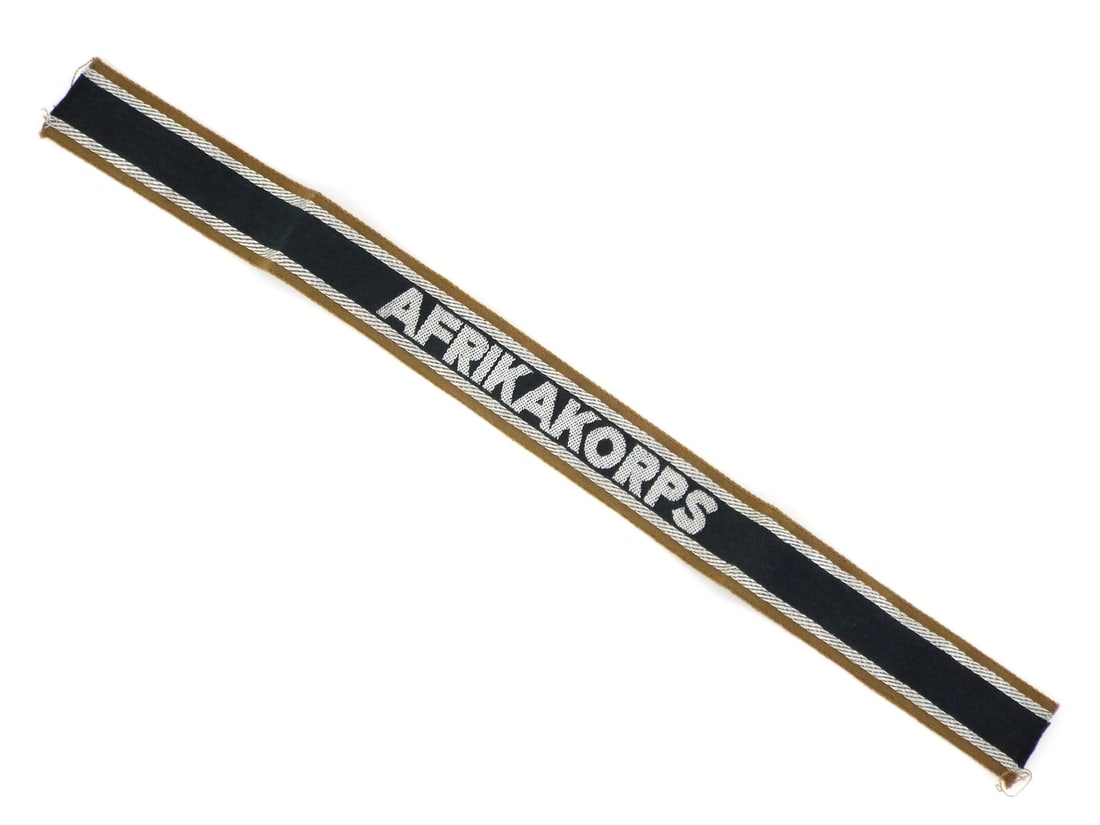 German WWII DAK AFRIKA KORPS CUFF TITLE Machine Woven Flatwire: Cotton body displays a deep forest green center stripe flanked by silver grey Russian braid borders, showing light toning and structural stability. The block lettering AFRIKAKORPS is rendered in a cri