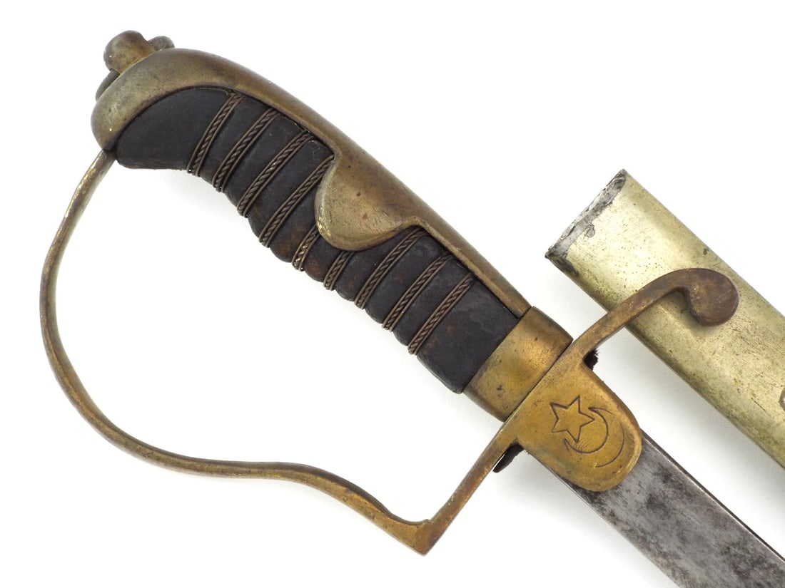 Ottoman WWI OFFICER SWORD with Scabbard: Single edged steel blade shows localized oxidation and age toning throughout. Ribbed grip remains tight with intact wire wrap, free of play. Matching brass mounted steel scabbard exhibits a dull patin