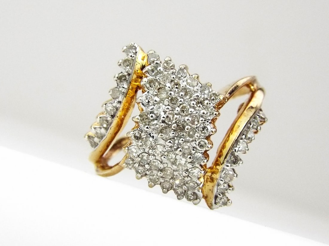 COCKTAIL RING 10K Yellow Gold: Tapered 10K yellow gold bypass shank exhibiting moderate surface patina. Tiered face features a dense cluster of prong set diamonds totaling 0.64 ctw. Solid construction weighing 3.4 grams with clear 
