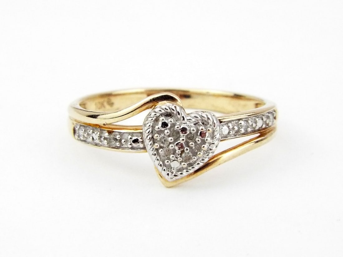 DIAMOND HEART BYPASS RING 10K Gold: Tapered 10K yellow gold bypass shank exhibits light surface wear and a clear hallmark. The central heart shaped cluster features a rope textured border housing approximately 0.20 ctw of diamond accent